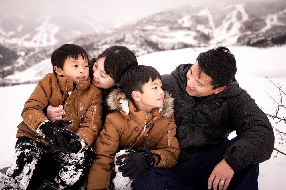 Two boys in brown coats  give their mom and dad a hug during a cold snowy day