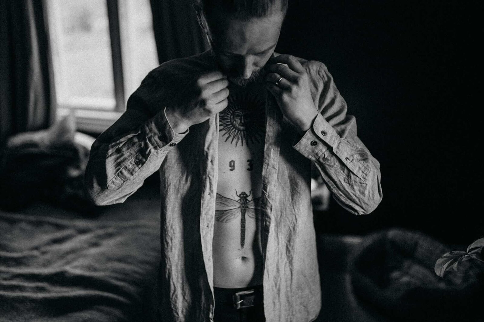 Tattooed groom getting ready in front of a window