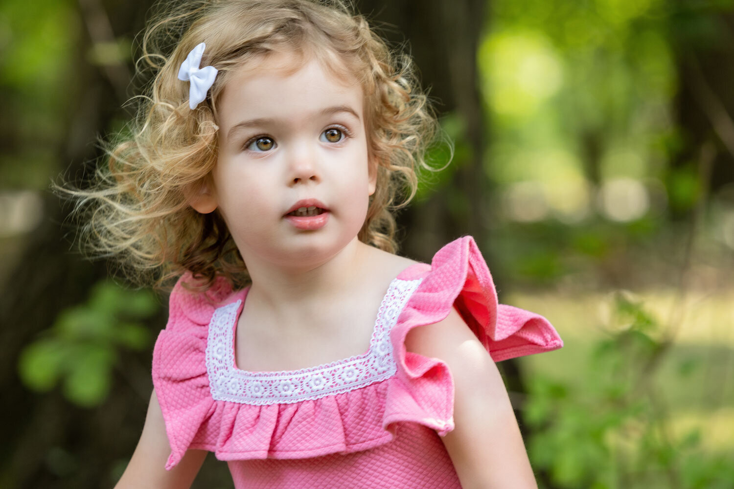 A little girl wearing a pink dress with ruffles and a bow in her hair