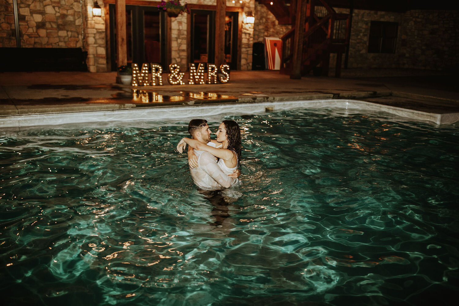 Bride and groom dipped in the pool hugging each other