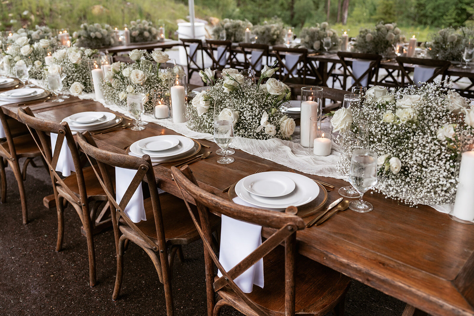Soft, natural light highlights a beautifully styled elopement table with wooden chairs, white florals, and glowing candles for an intimate celebration.
