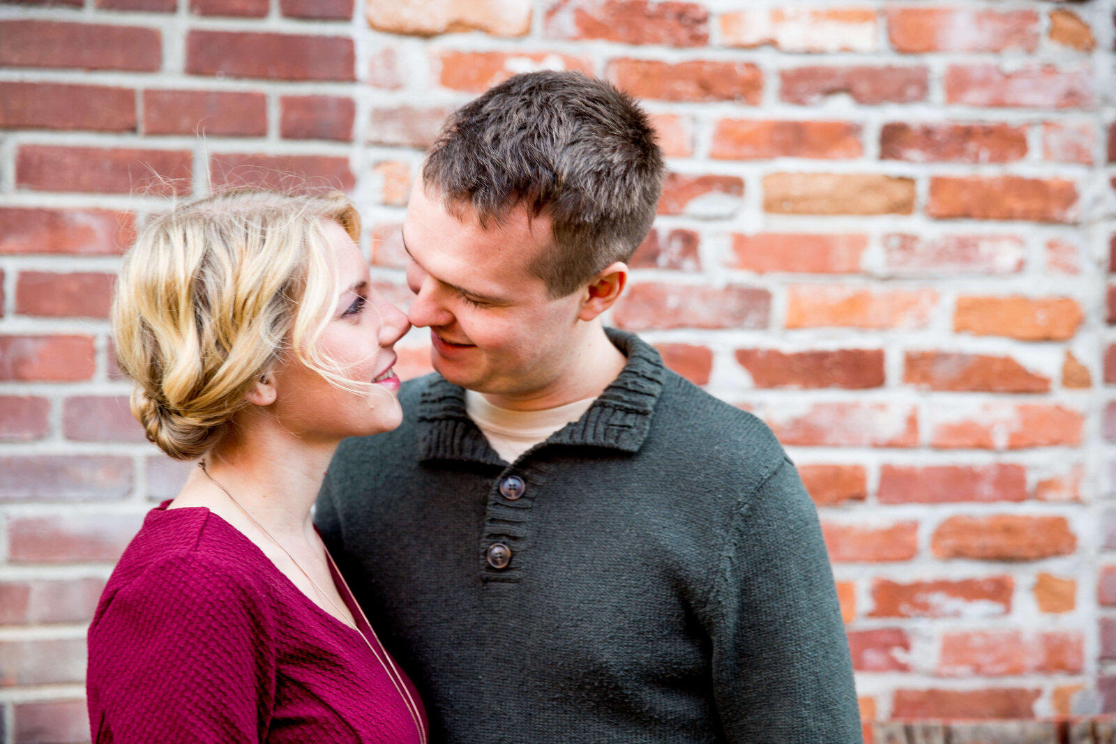 Couple smile at each other with brick background.