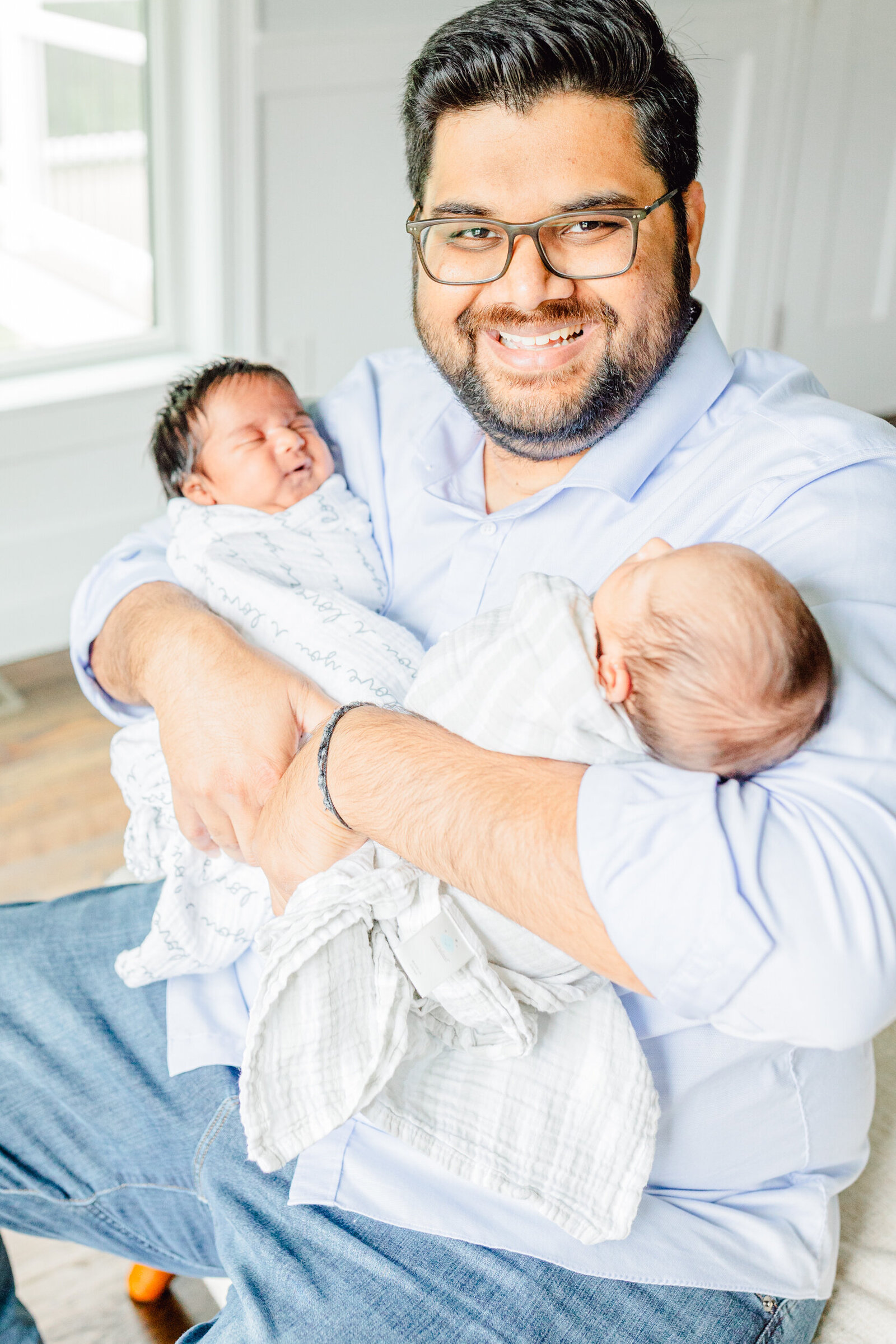 Dad smiles proudly with a newborn in each arm