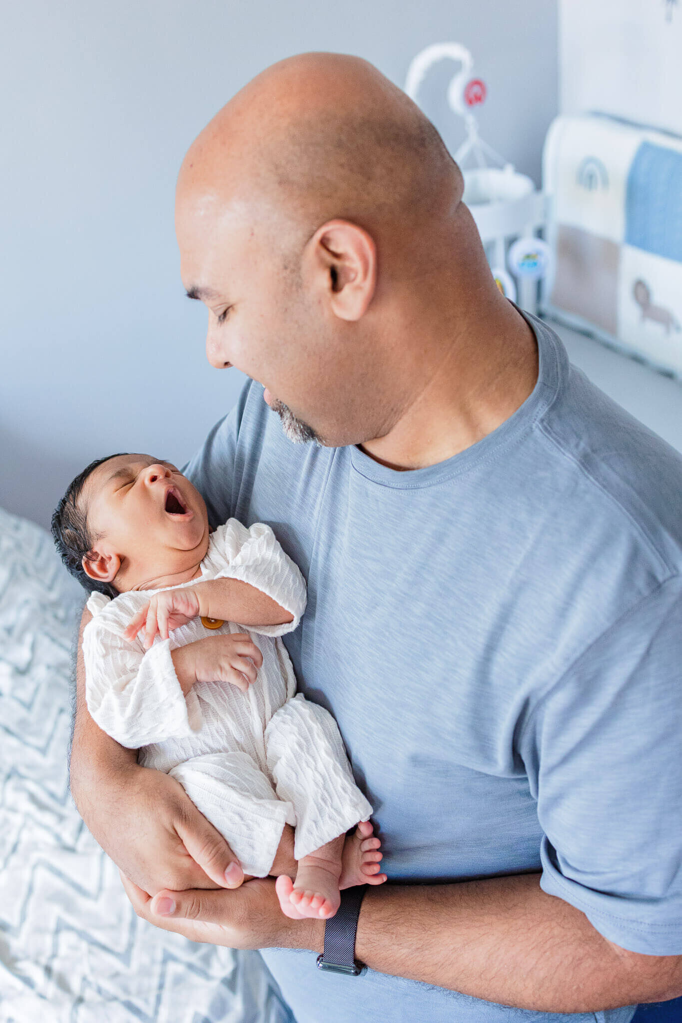 A newborn boy being held by his dad and yawning.