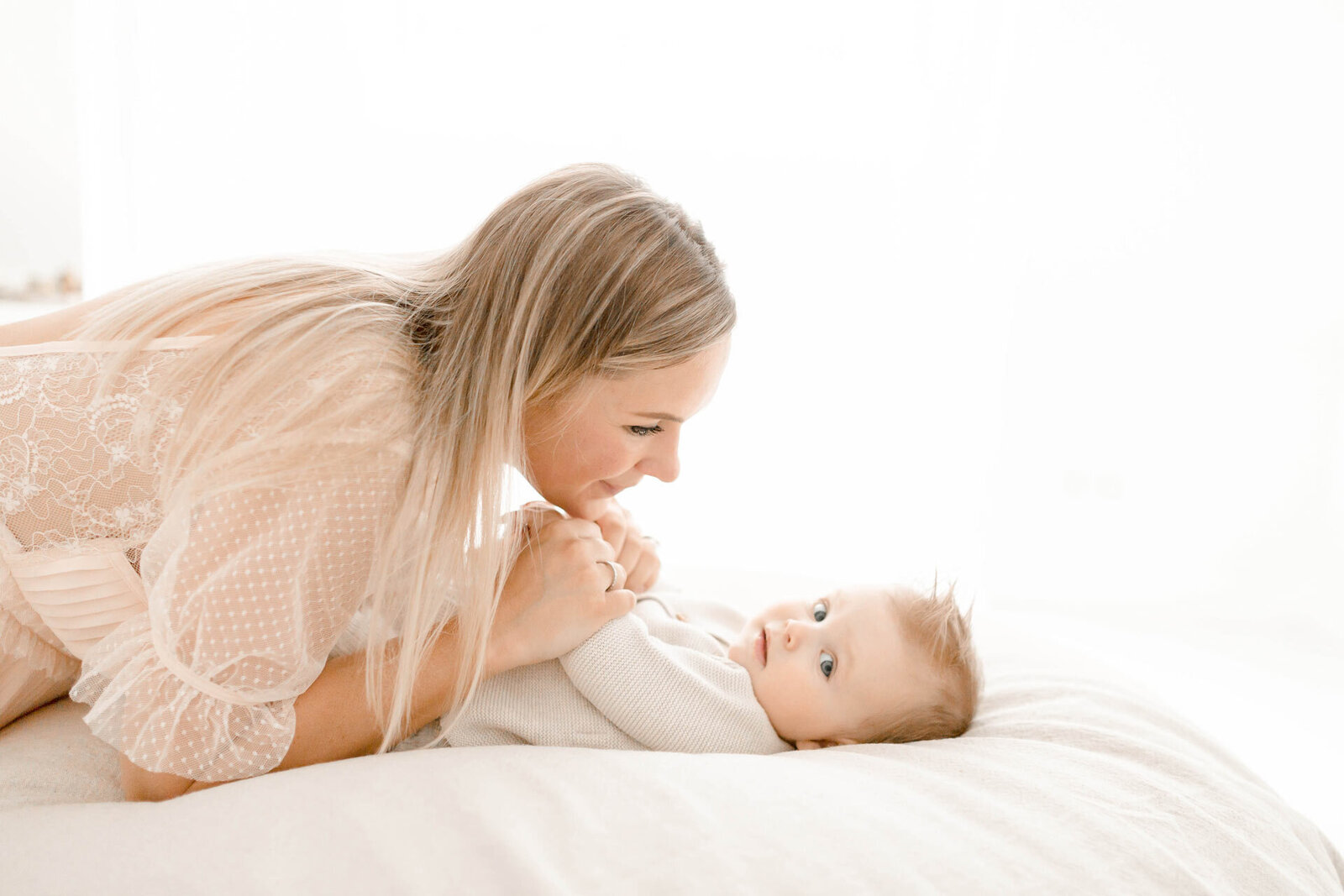 Liebevolle Babyfotografie von Babyfotografin Josephine Boeck in Gütersloh bei Bielefeld. Mama ist über ihr Baby gebeugt,  hält seine Hände und blickt ihn liebevoll an.