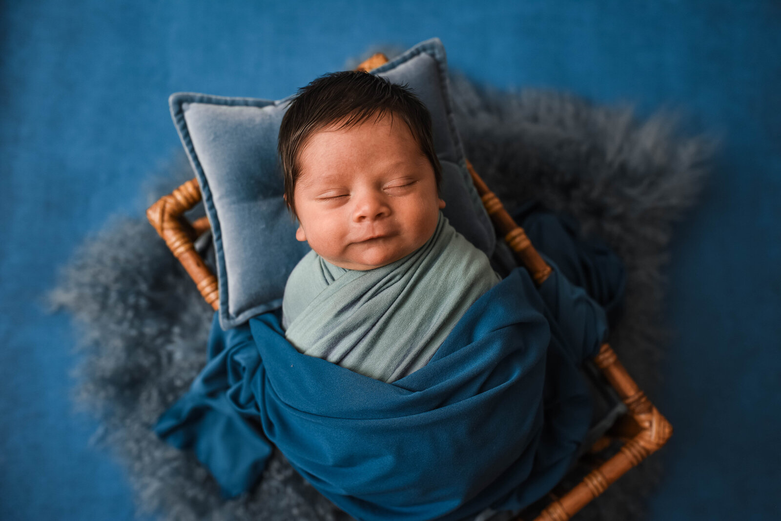 newborn laying in wooden box wrapped in blue blanket laying on blue pillow