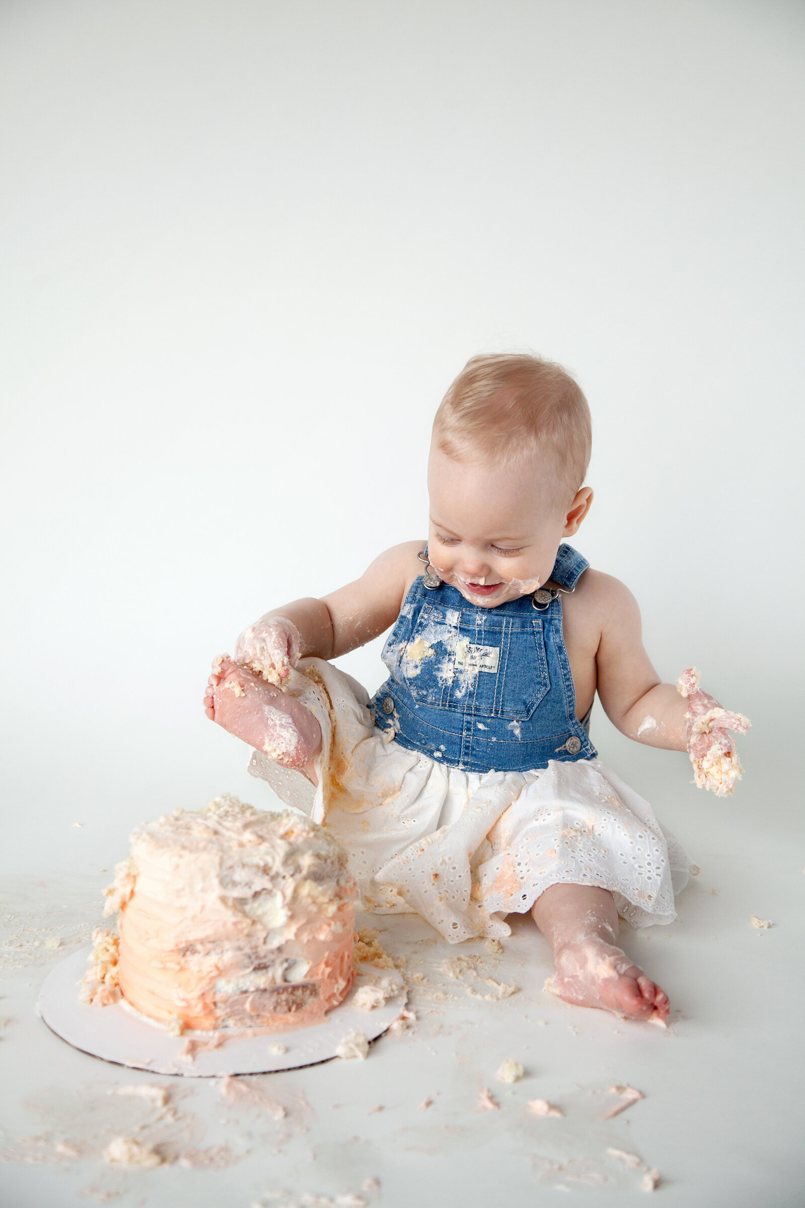 One year old in dress putting her foot in smash cake.