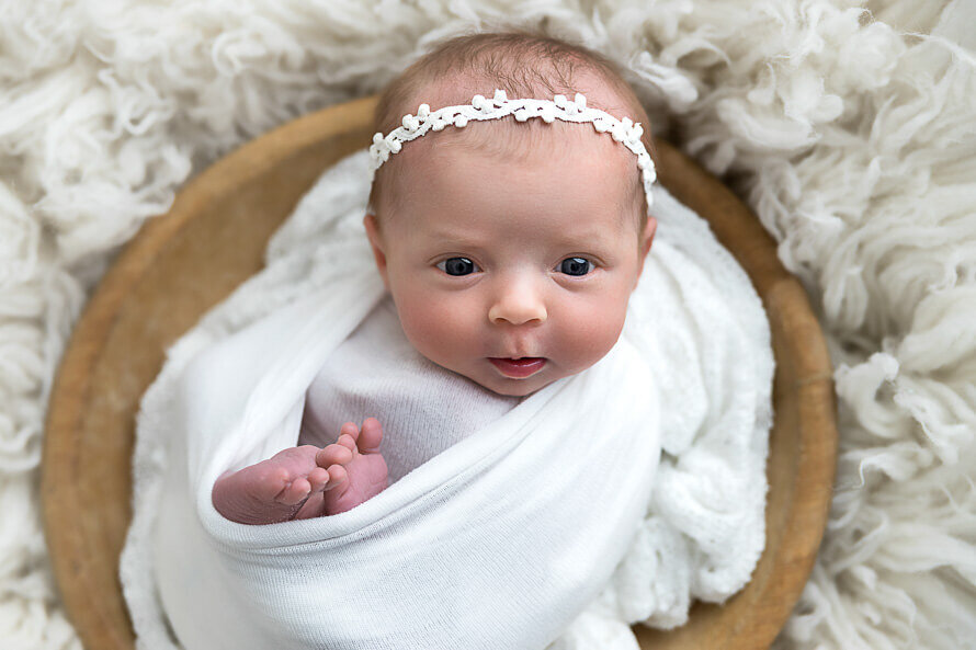 Newborn wrapped in a bowl looks at camera, with her toes sticking out.