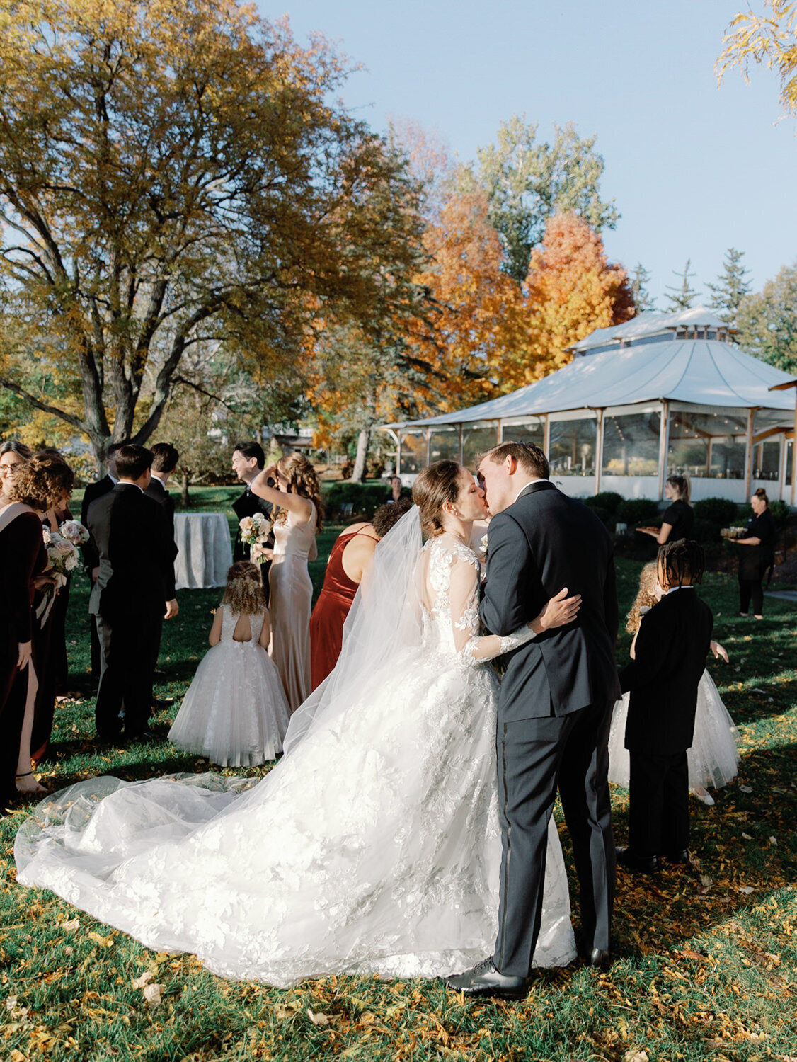 Bride and groom share a kiss with guests in the background.