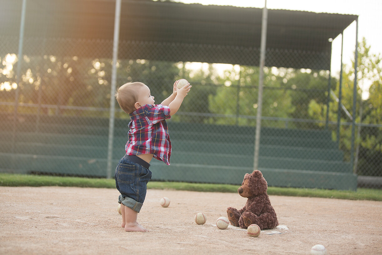 Baby boy with teddy bears on Austin baseball field.