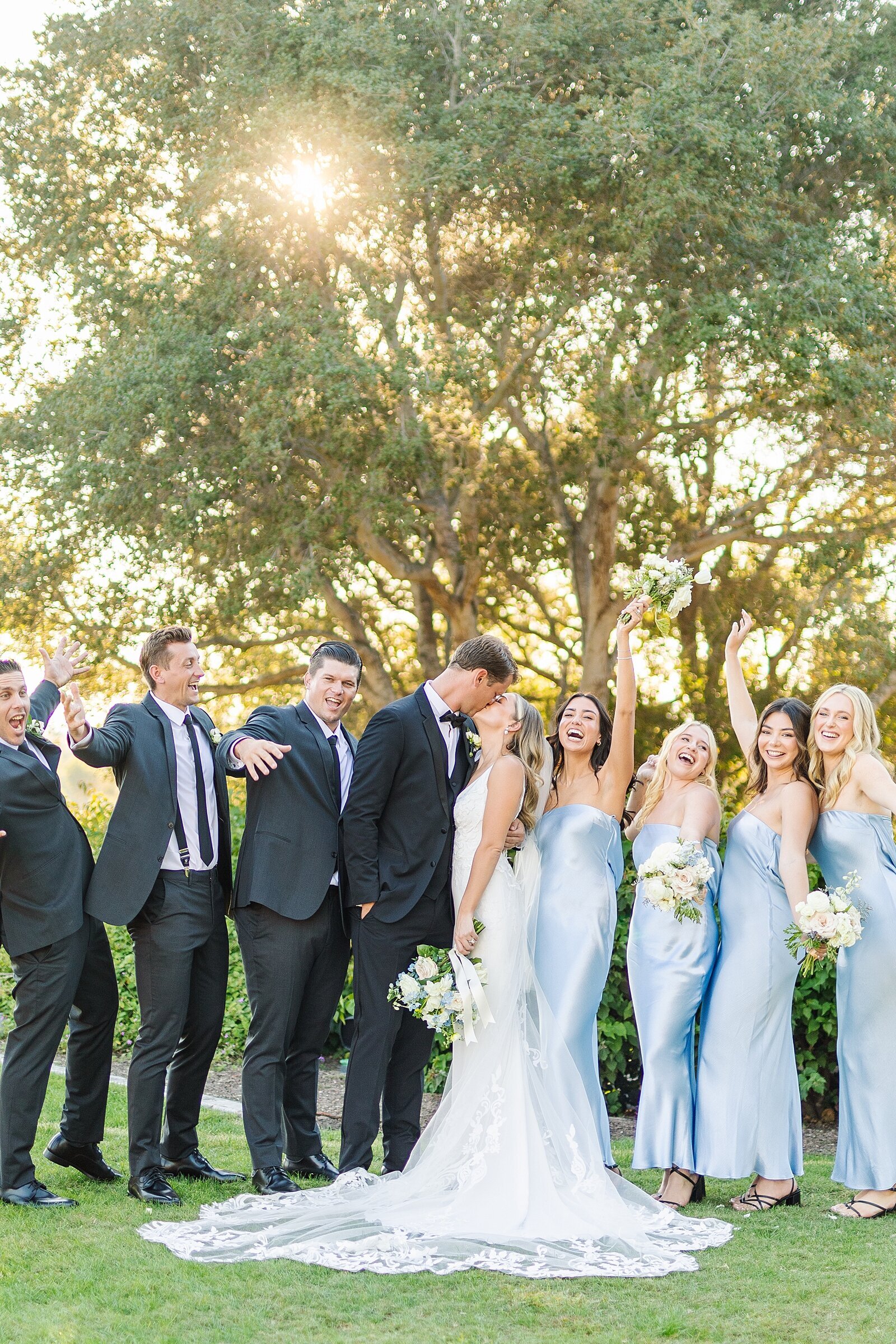 Bride and groom kissing while bridesmaids and groomsmen cheer at Rancho Valencia in Rancho Sante Fe photographed by Sherr Weddings.