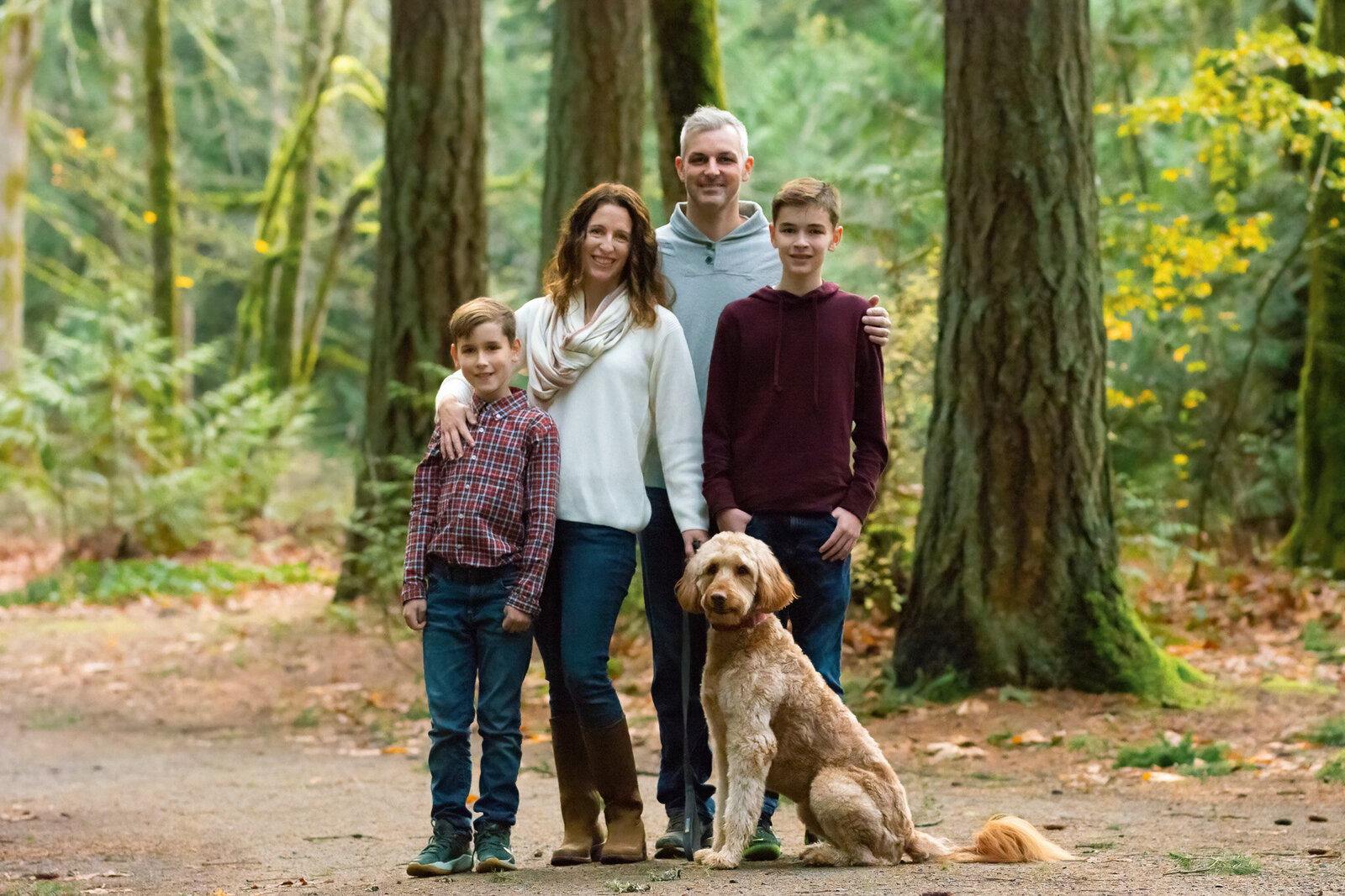 Family with two boys and their golden doodle dog posing together in a forest during a Colorado outdoor family portraits session.