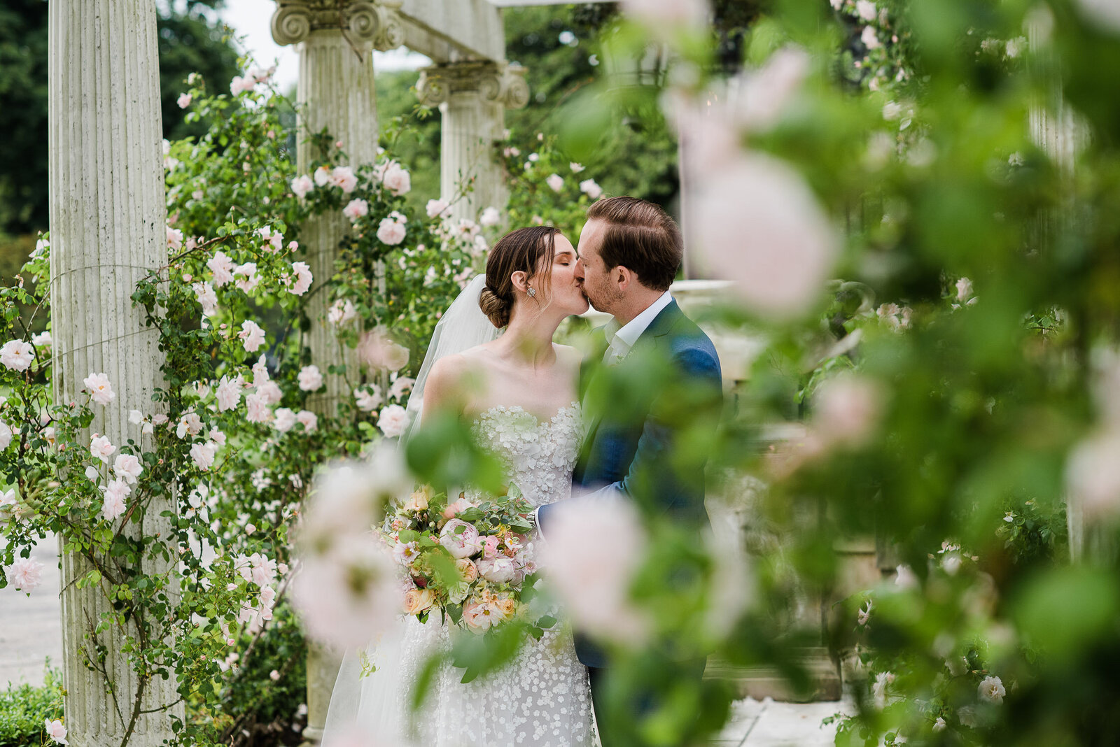 bride and groom kiss behind rose bushes