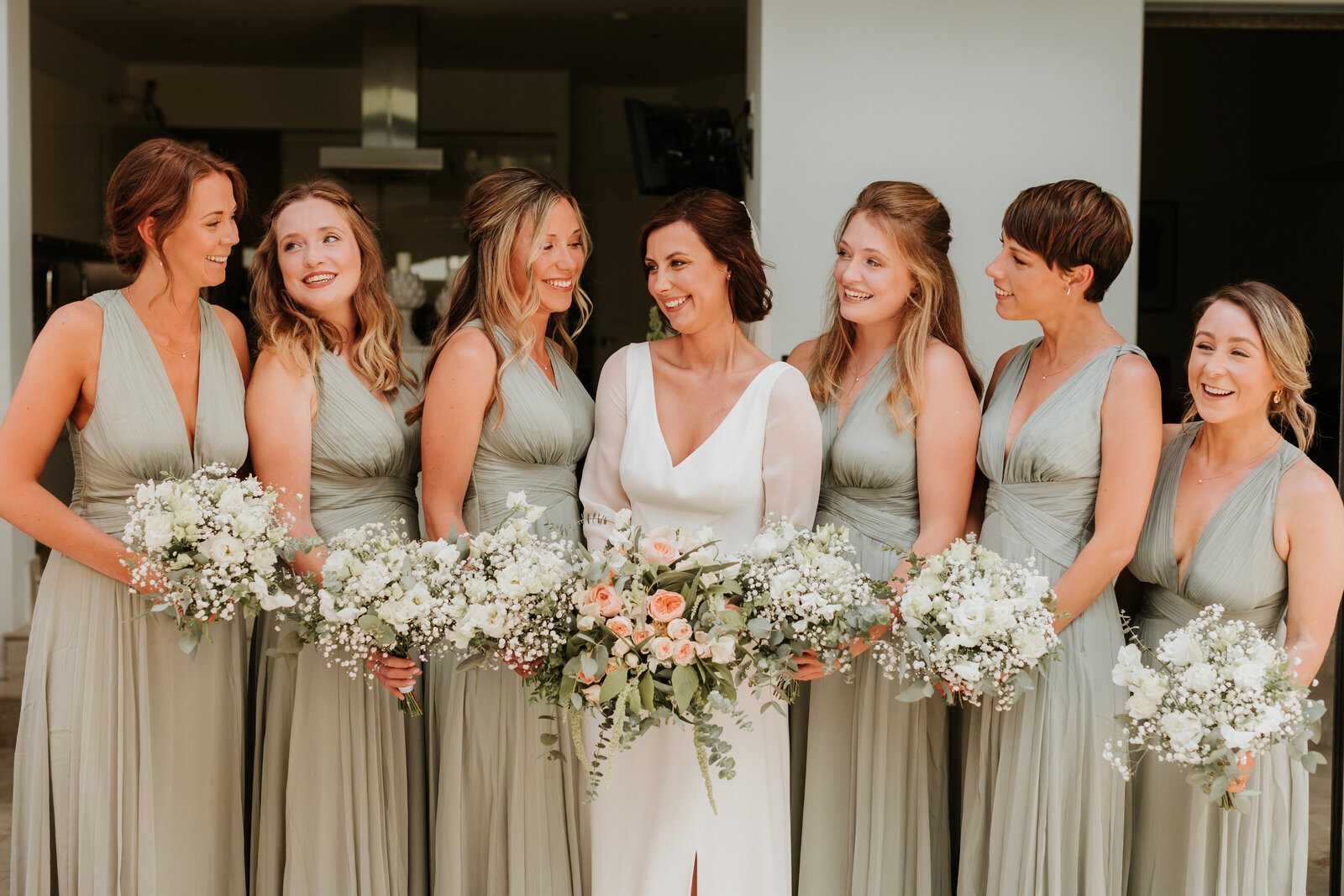 Bridesmaids in light green dresses smiling at the bride.