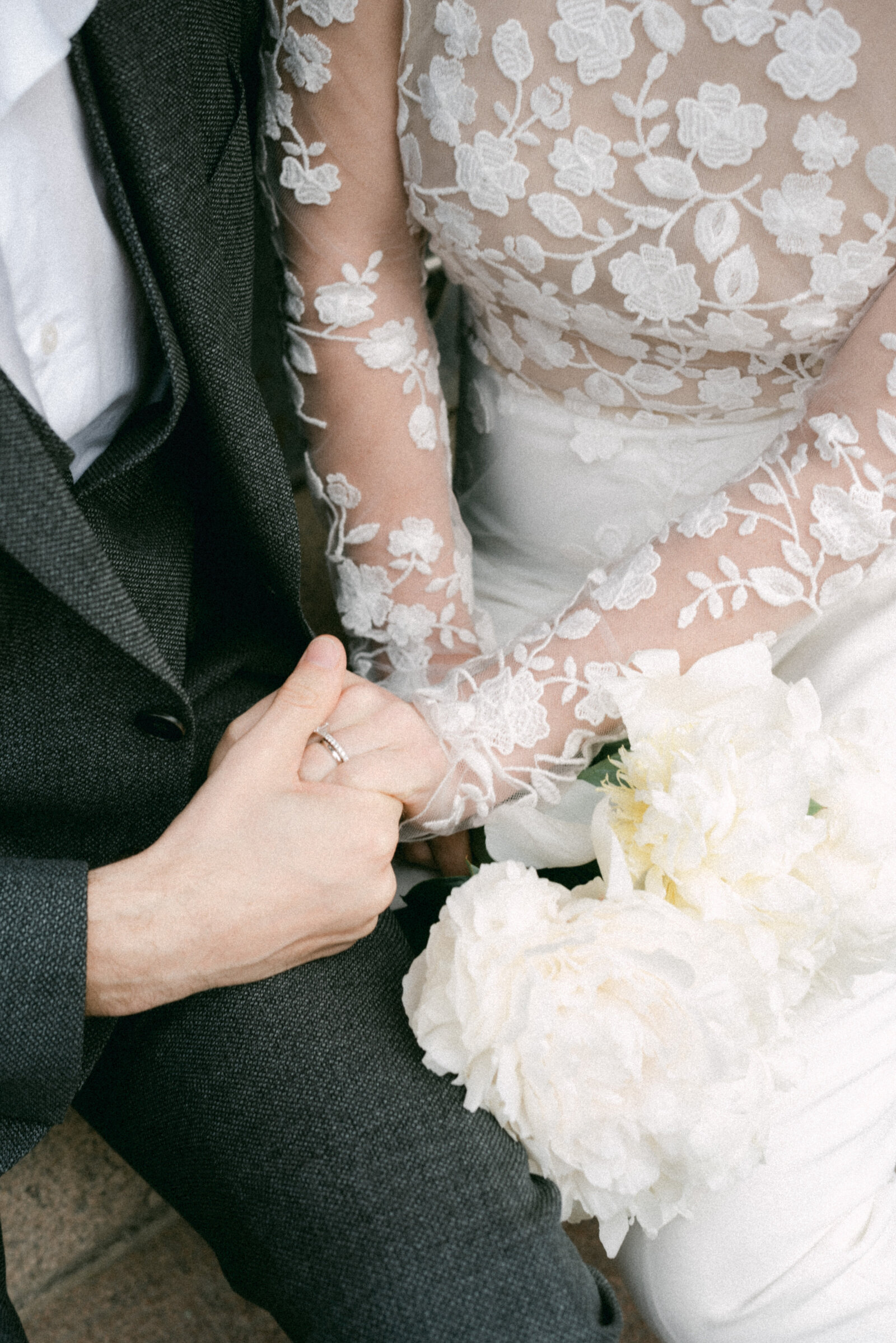 Detail image of a wedding couple holding hands. The bride has a bouquet of white peonies on her lap. Image by the wedding photographer Hannika Gabrielsson.
