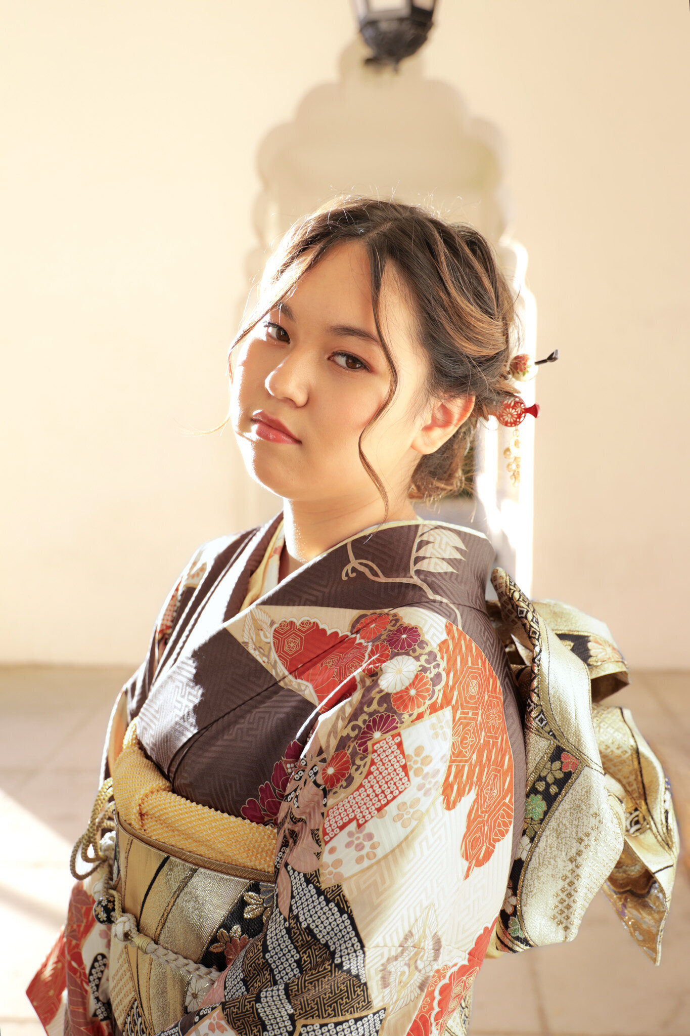 Young woman in a rich brown and gold furisode captured during golden-hour light at Brand Park Los Angeles for a Seijinshiki (coming-of-age) celebration kimono rental | ロサンゼルス・ブランドパークで夕陽に包まれた成人式の振袖姿の女性。お祝いの着物レンタル
