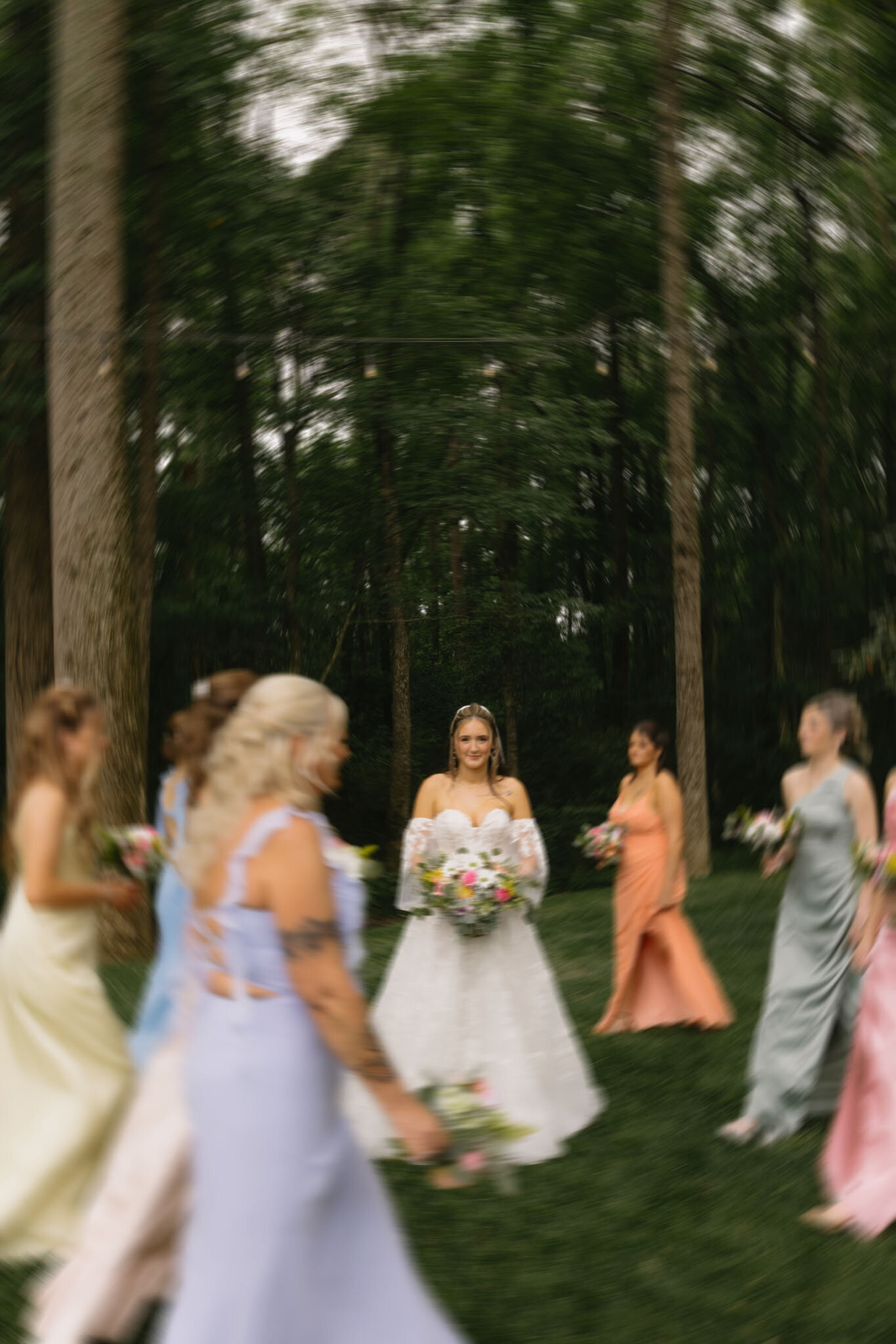 Bride standing  and holding a floral bouquet while guests walk past in motion blur