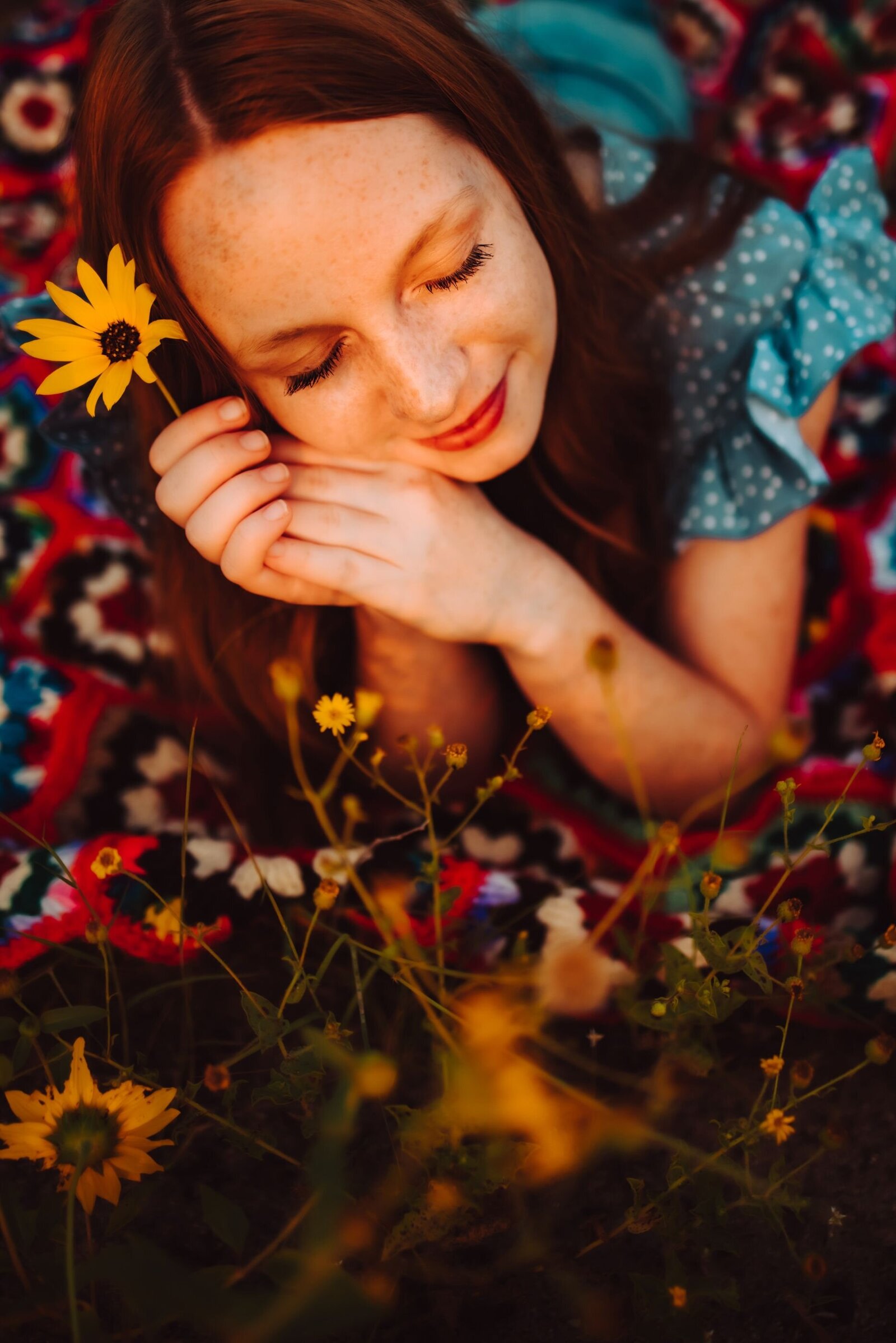 A young woman laying on a blanket in a field of yellow flowers. Her eyes are closed and her head is resting on her hands, in one hand she is holding a yellow flower. captured by Infinite Productions