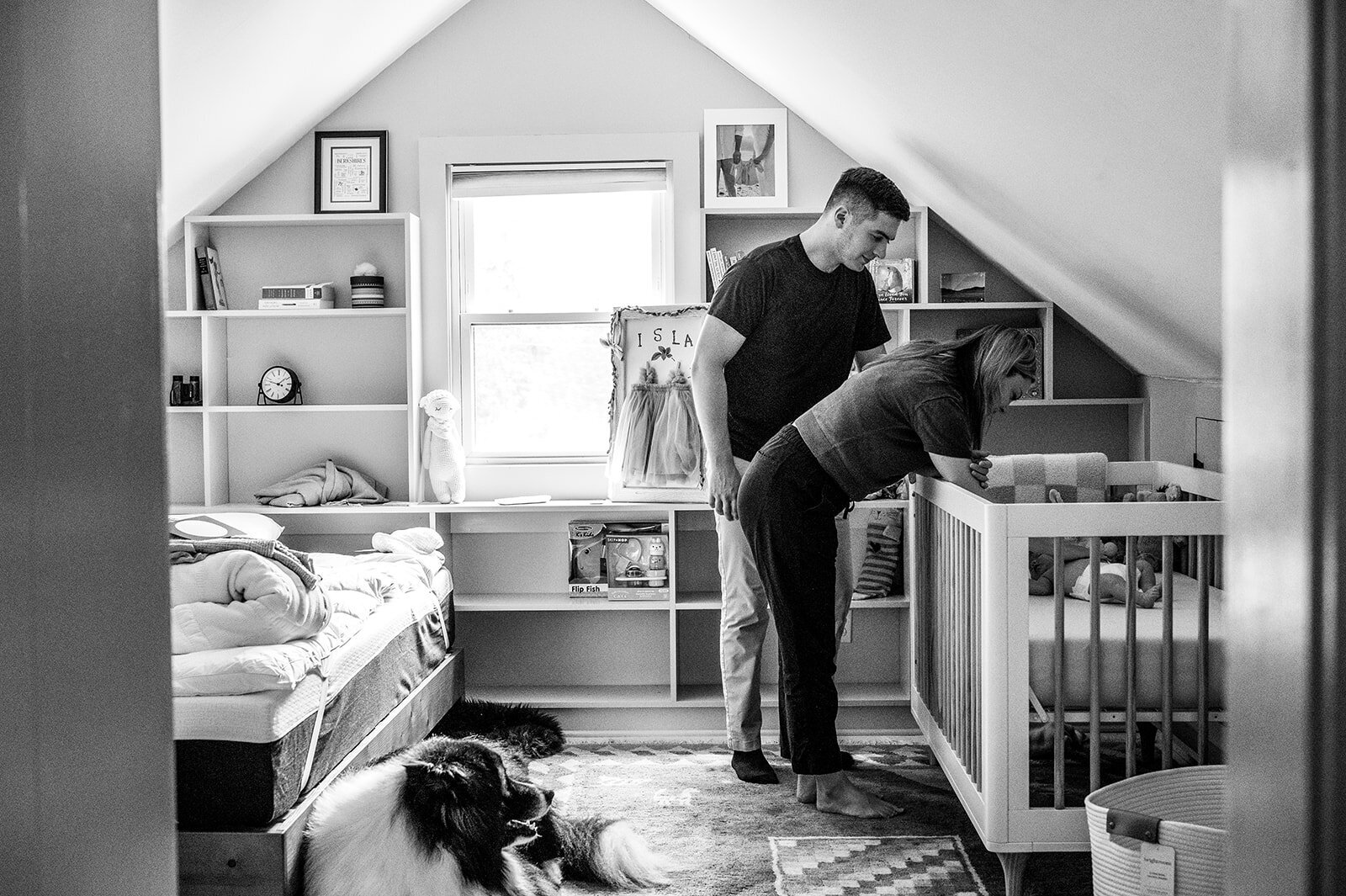 Mother holding smiling newborn to her chest while father listens and smiles during a candid in-home moment