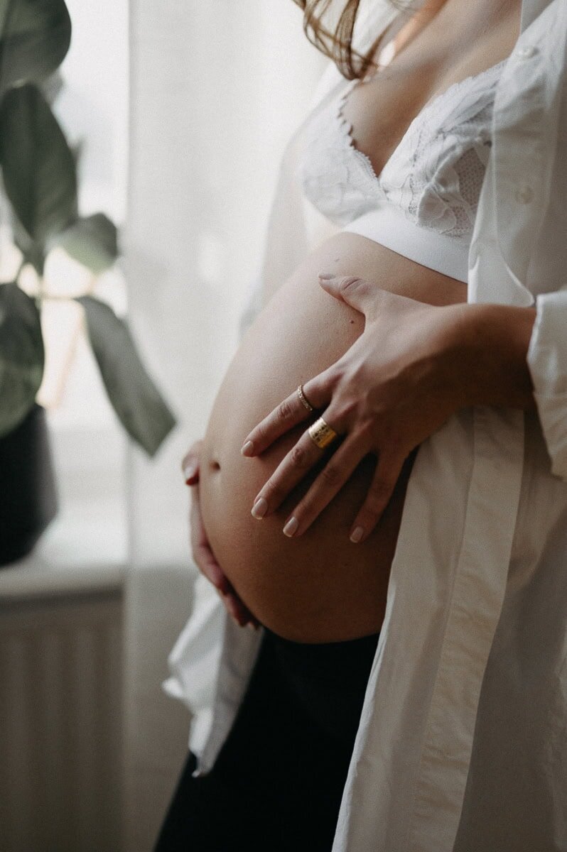 Gravid kvinna håller om sin växande mage i öppen skjorta.