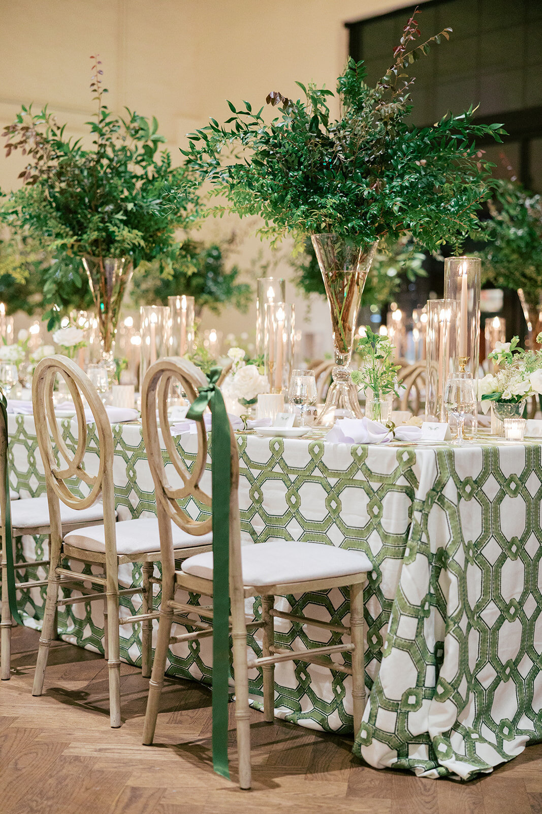 candlelit reception table withgreen and white table cloth and setting, tan chairs with green bow tied on 