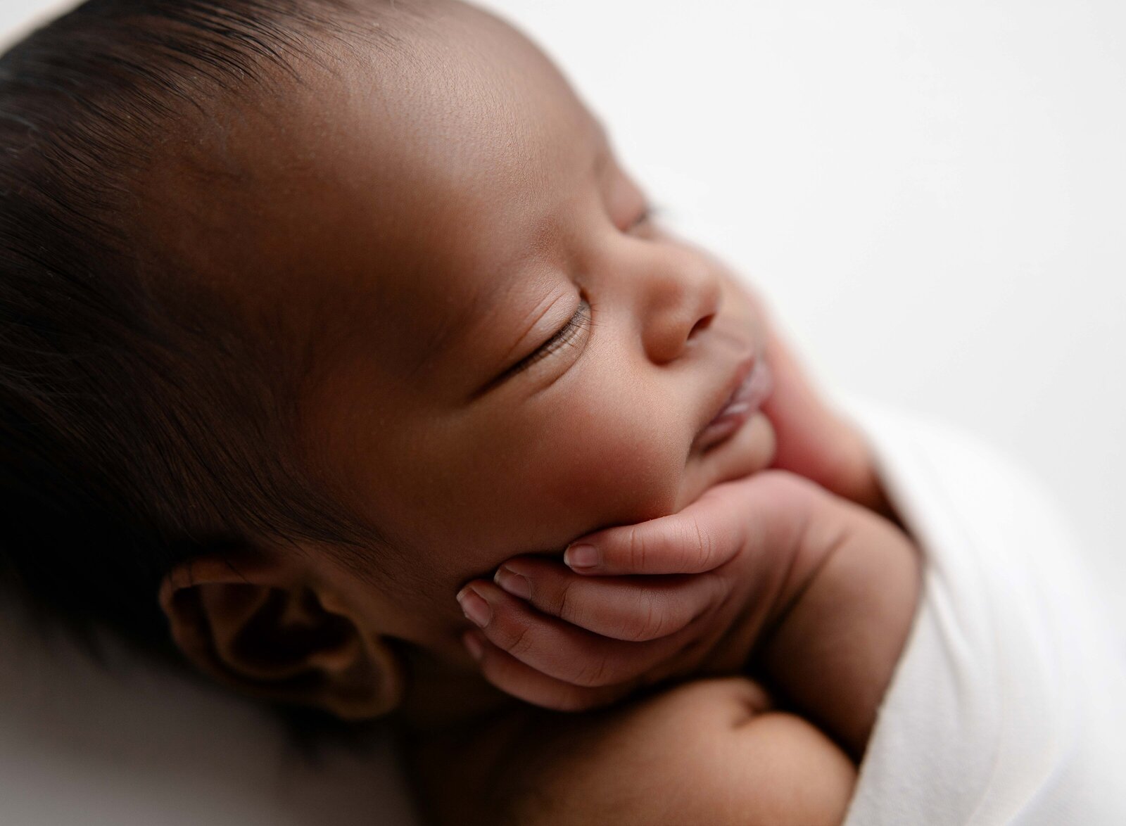 Macro photo of baby boy's face with his hands on cheek. Newborn Photography session photographed at Jenni Nikki's photo studio in Marietta, GA.