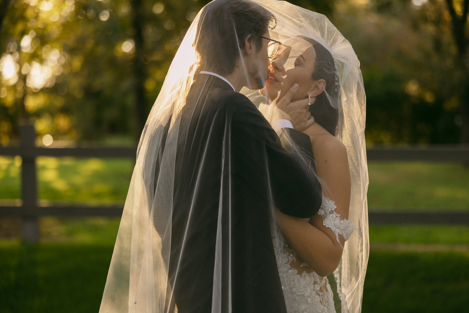 A bride and groom kissing with a veil over their heads.