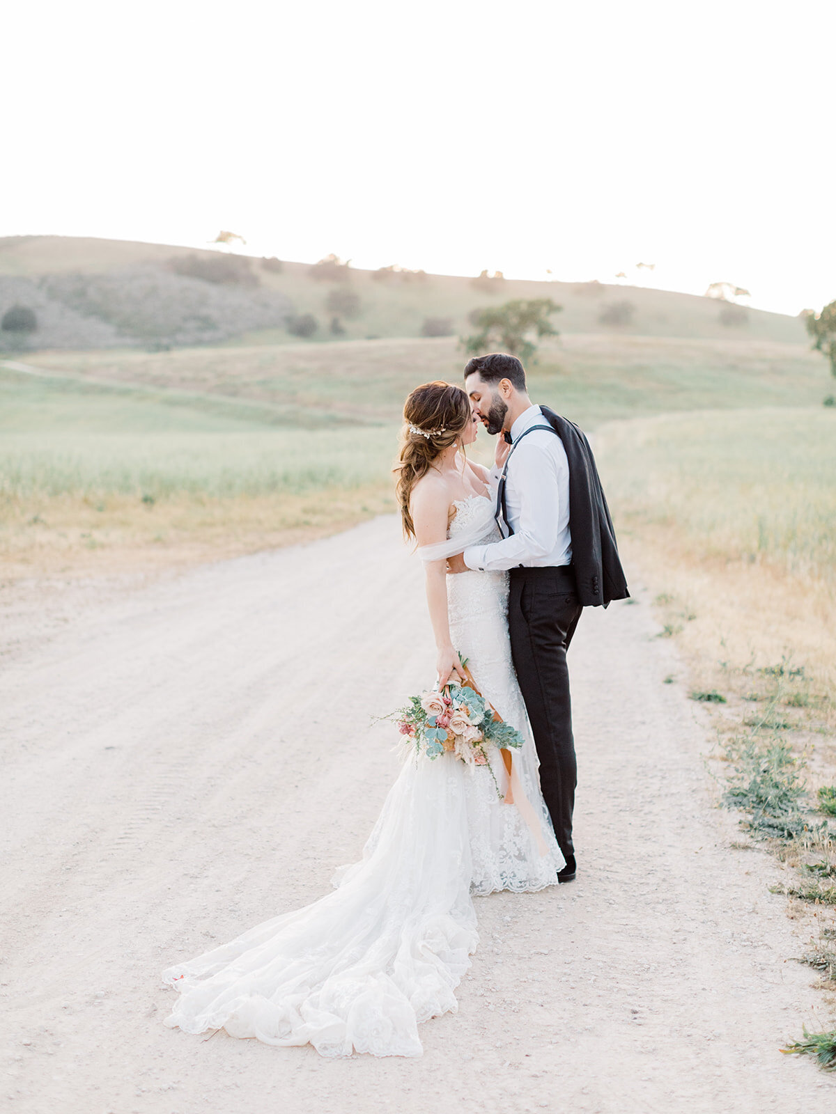 bride and groom standing on a dirt road through field and kissing