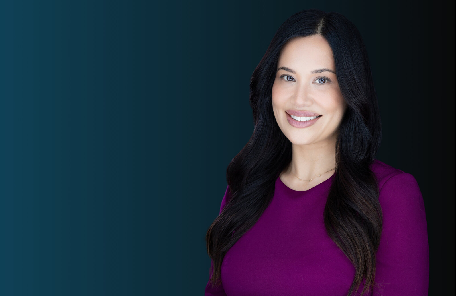 Woman with black long hair and perfect makeup looks at the camera and smiles for a business headshot in Sacramento headshot Studio