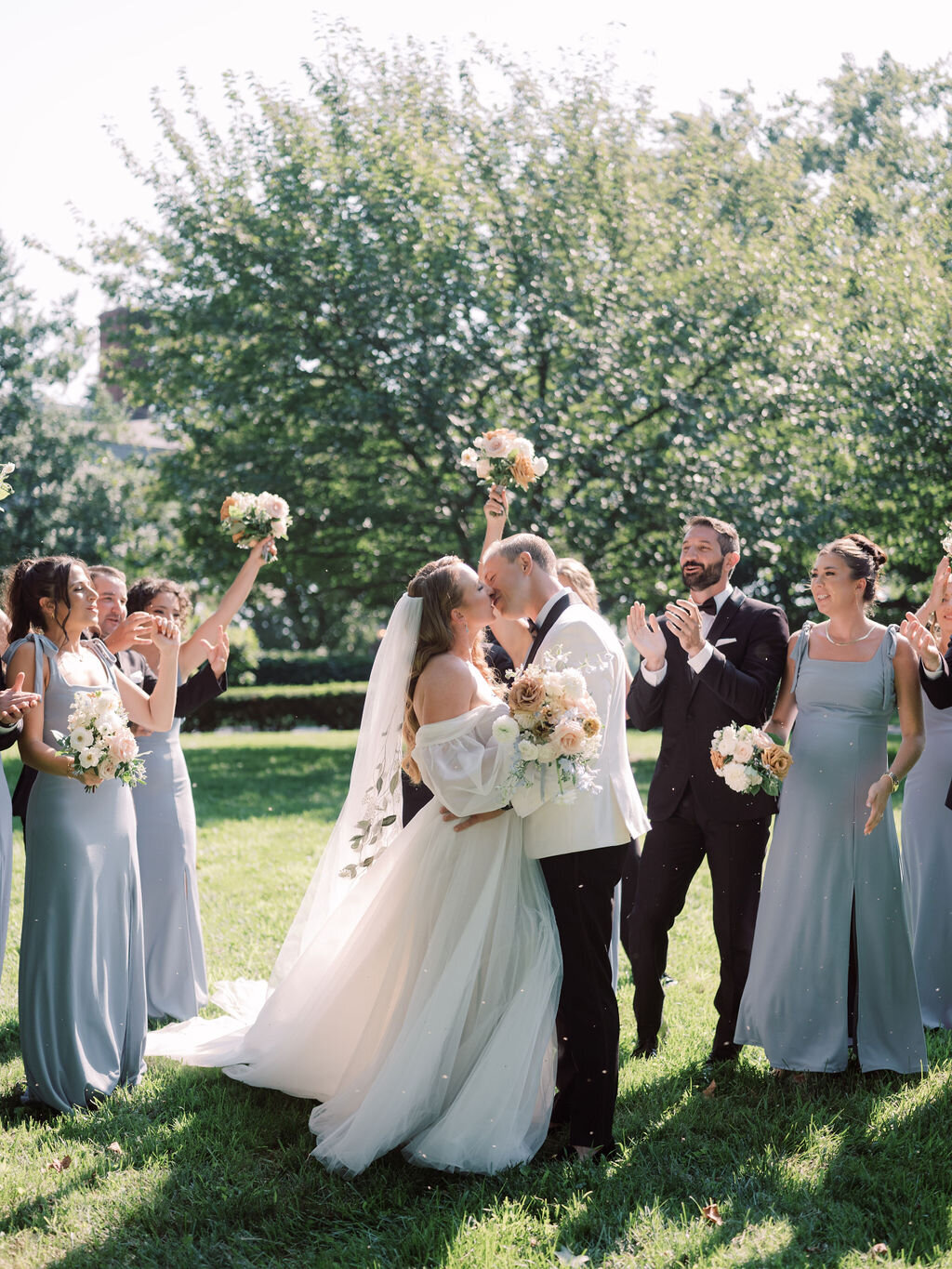 Bride and groom kissing in front of bridal party wearing a white tuxedo and light blue dresses