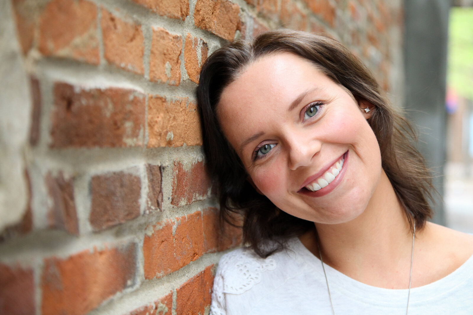 Close up of woman leaning head against brick building, smiling.