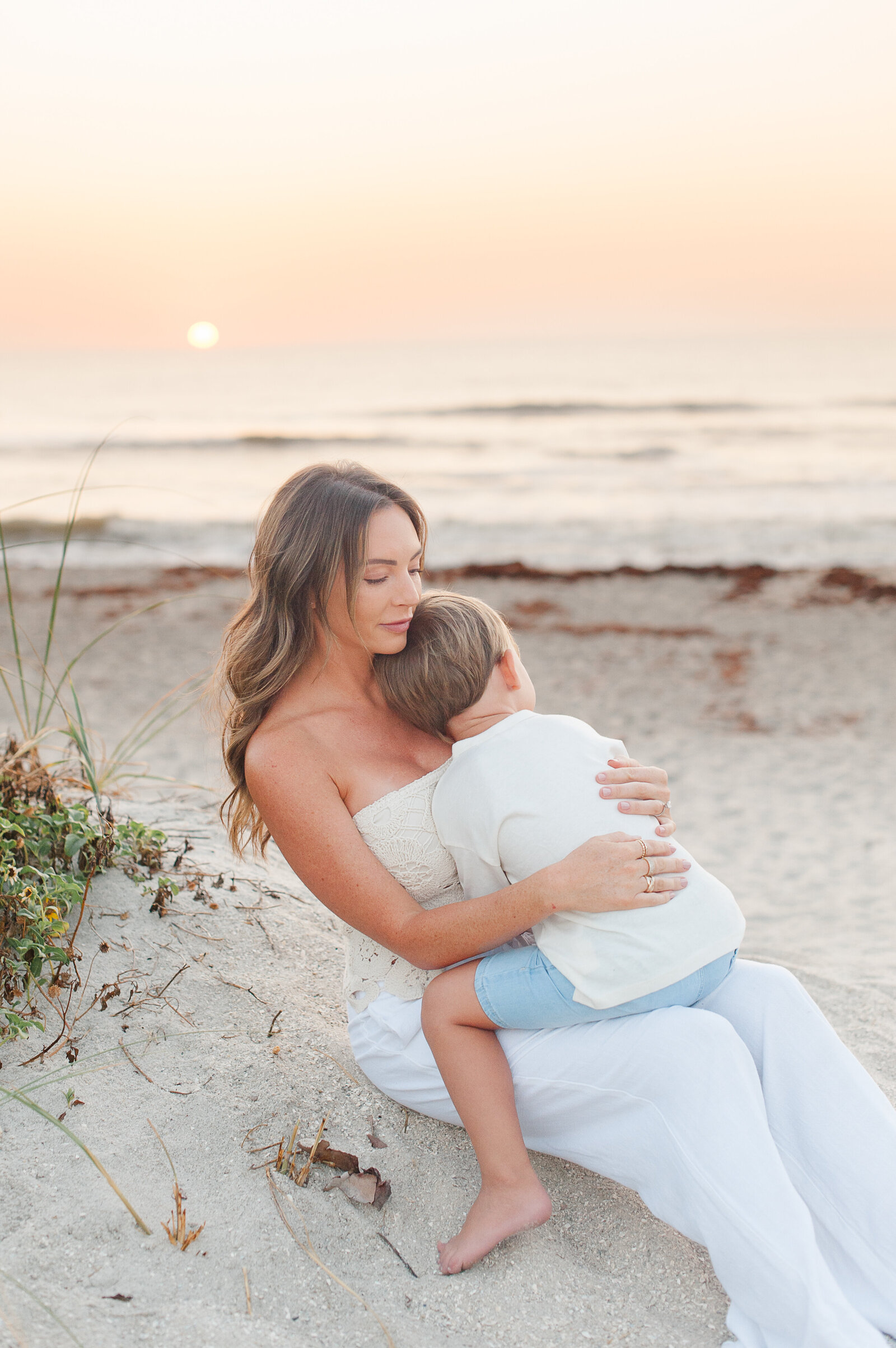 Mother holding her son on the beach at sunrise