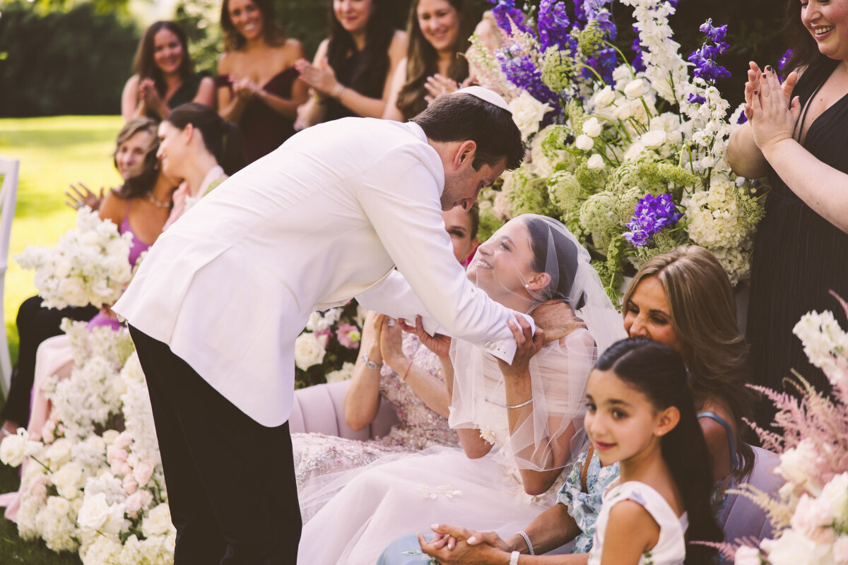 Newlyweds kissing during their Jewish ceremony at Tanglewood as family gathers around them