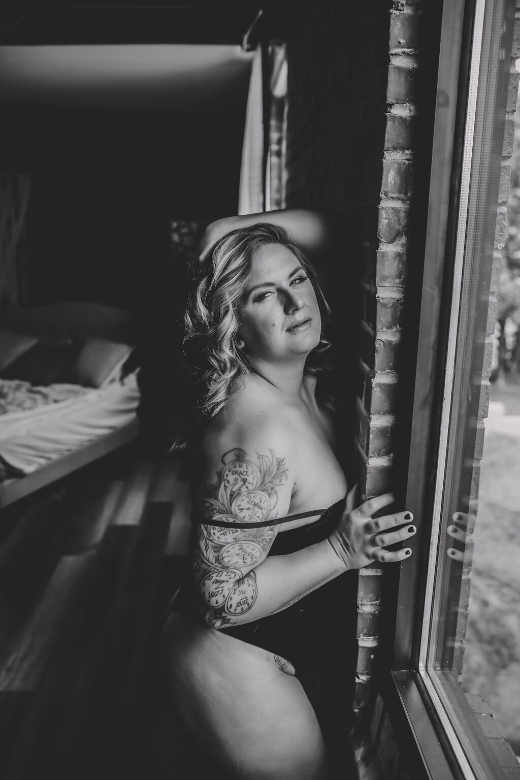 close up black and white portrait boudoir of woman in lingerie with hand in hair by window