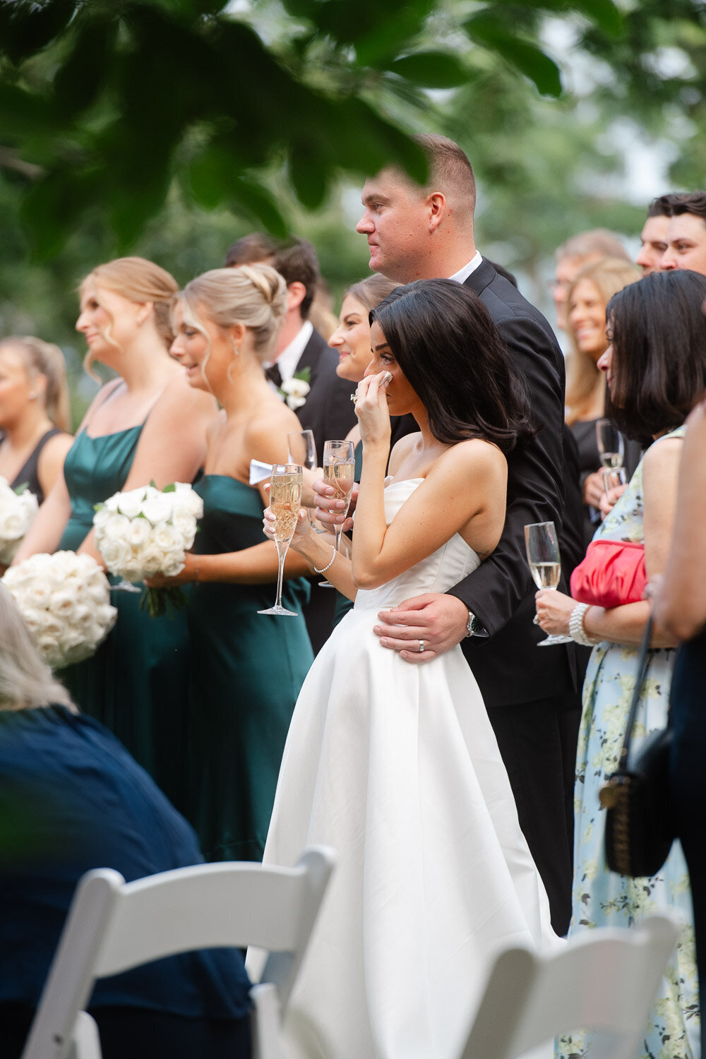 bride wiping tears during toasts in group of guests