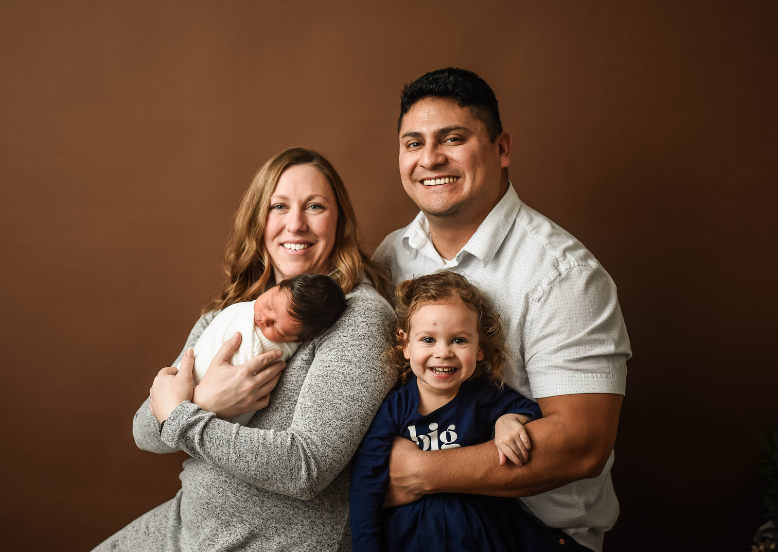 a mother and father sitting for a photo session with their toddler and newborn child