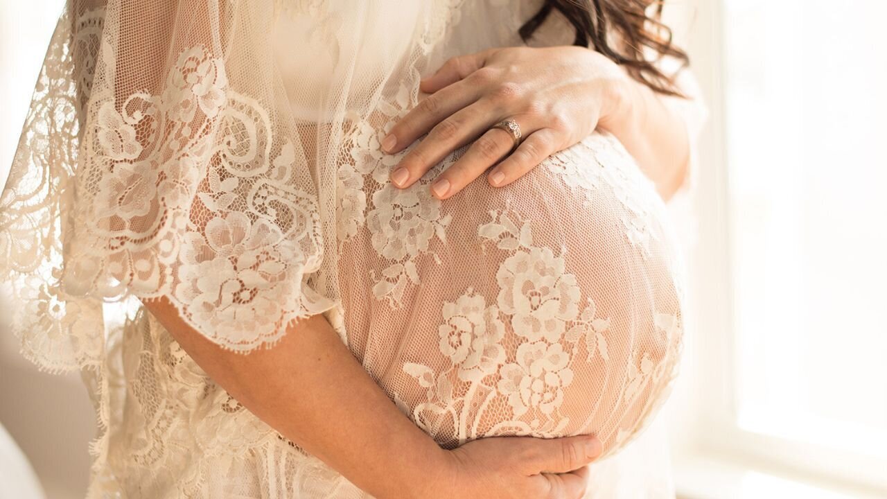 Soft lace drapes over a mother’s belly in a glowing maternity portrait. A timeless maternity session by Moments in Light Photography.