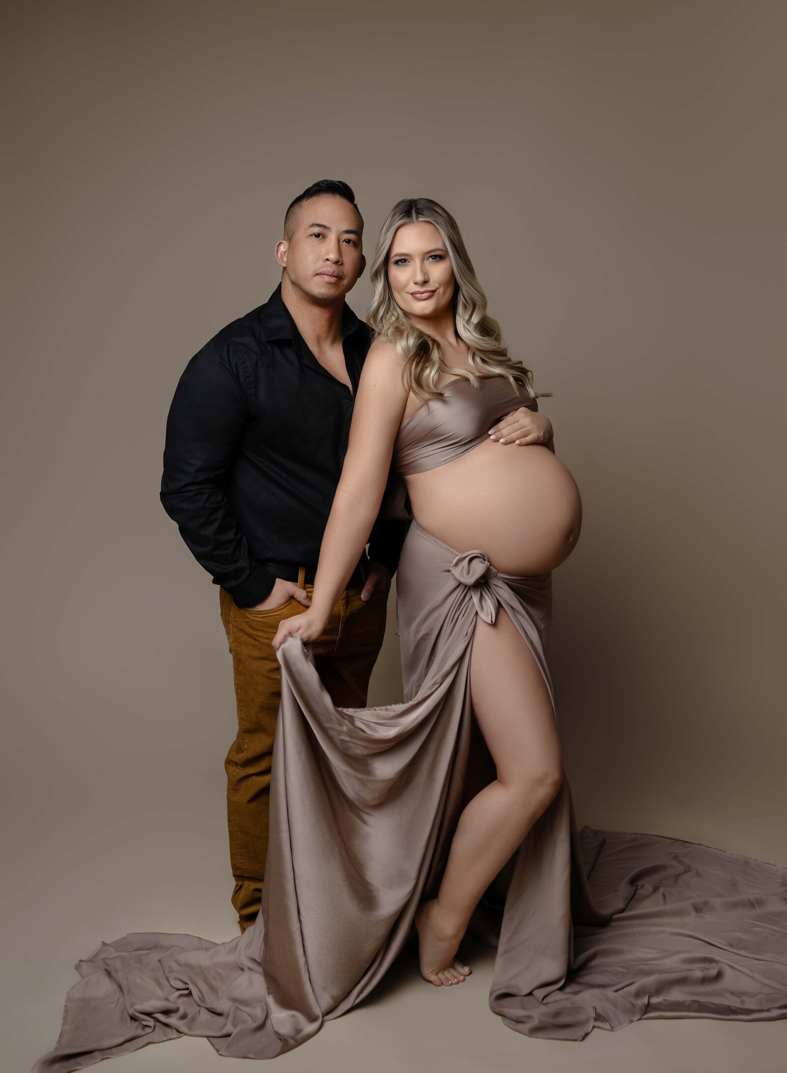 Mom holding draped skirt and Dad with hand in pocking, both posing and looking at camera. Maternity portrait taken by Jenni. Nikki Photography at Atlanta Photo Studio. 