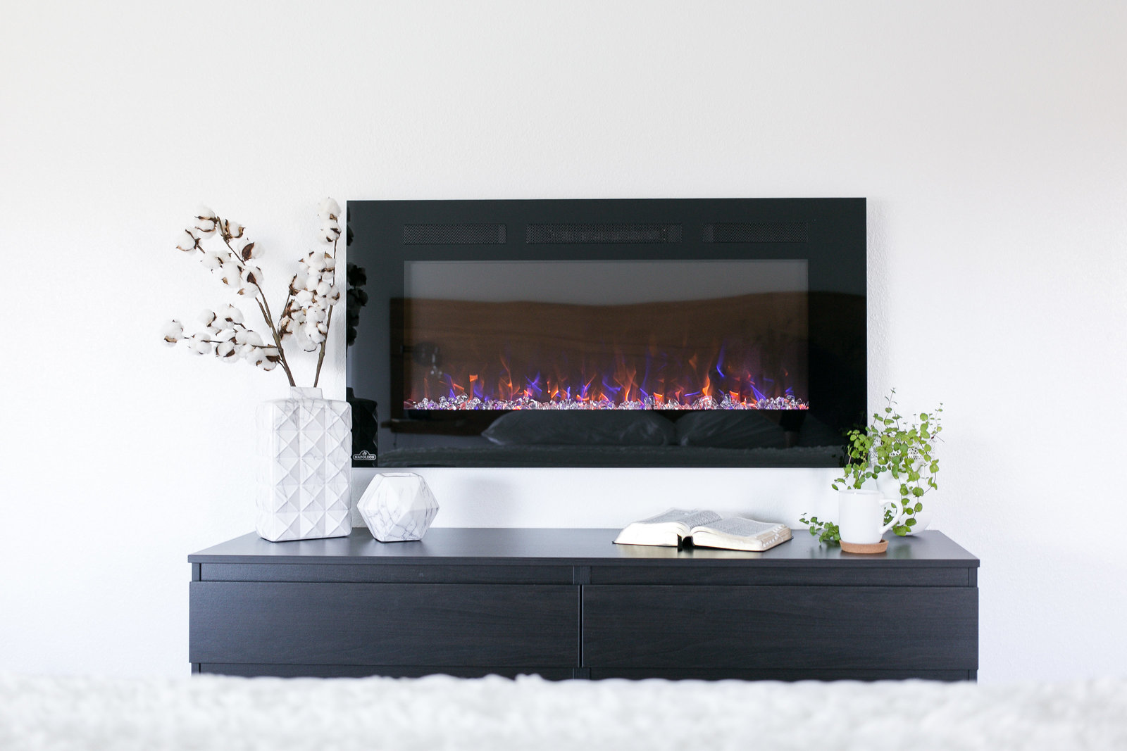 Modern BnB Master Bedroom design with hanging fireplace, black dresser for storage and minimalistic decor.