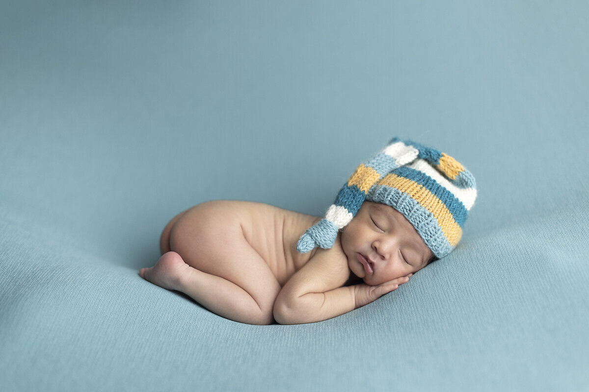 ewborn boy curled up on blue fabric, posed by a Dallas newborn photographer.