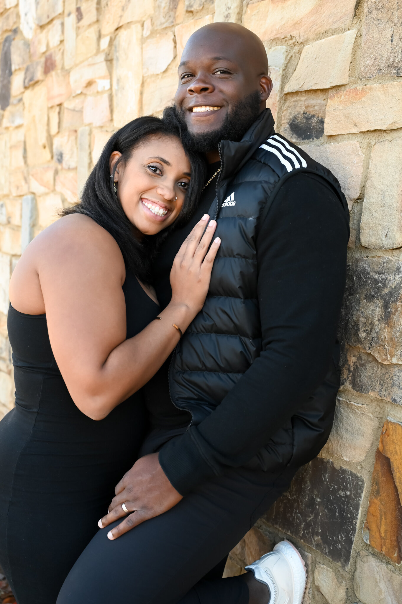 a woman leaning her chest and hands on the chest of her boyfriend as he leans against a brick wall. photographed by Millz Photography in Greenville, SC