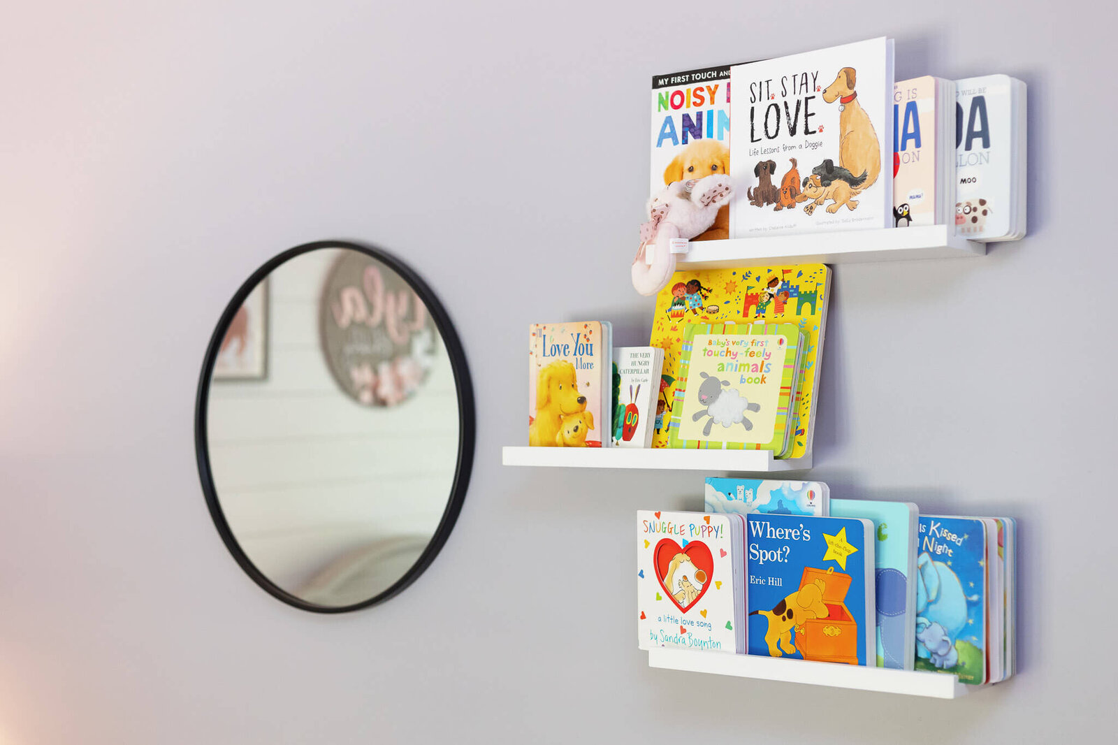A set of three floating bookshelves on the wall filled with books and a mirror hanging on the wall.