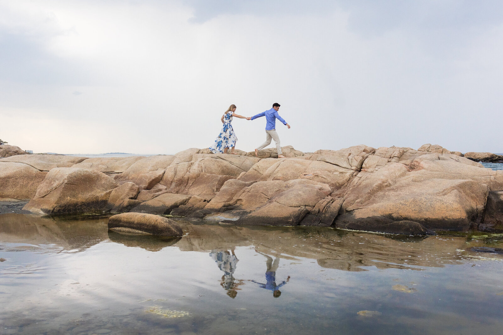 coastal-engagement-couple-runs-on-rocks-reflection-lisa-gilbert-photography