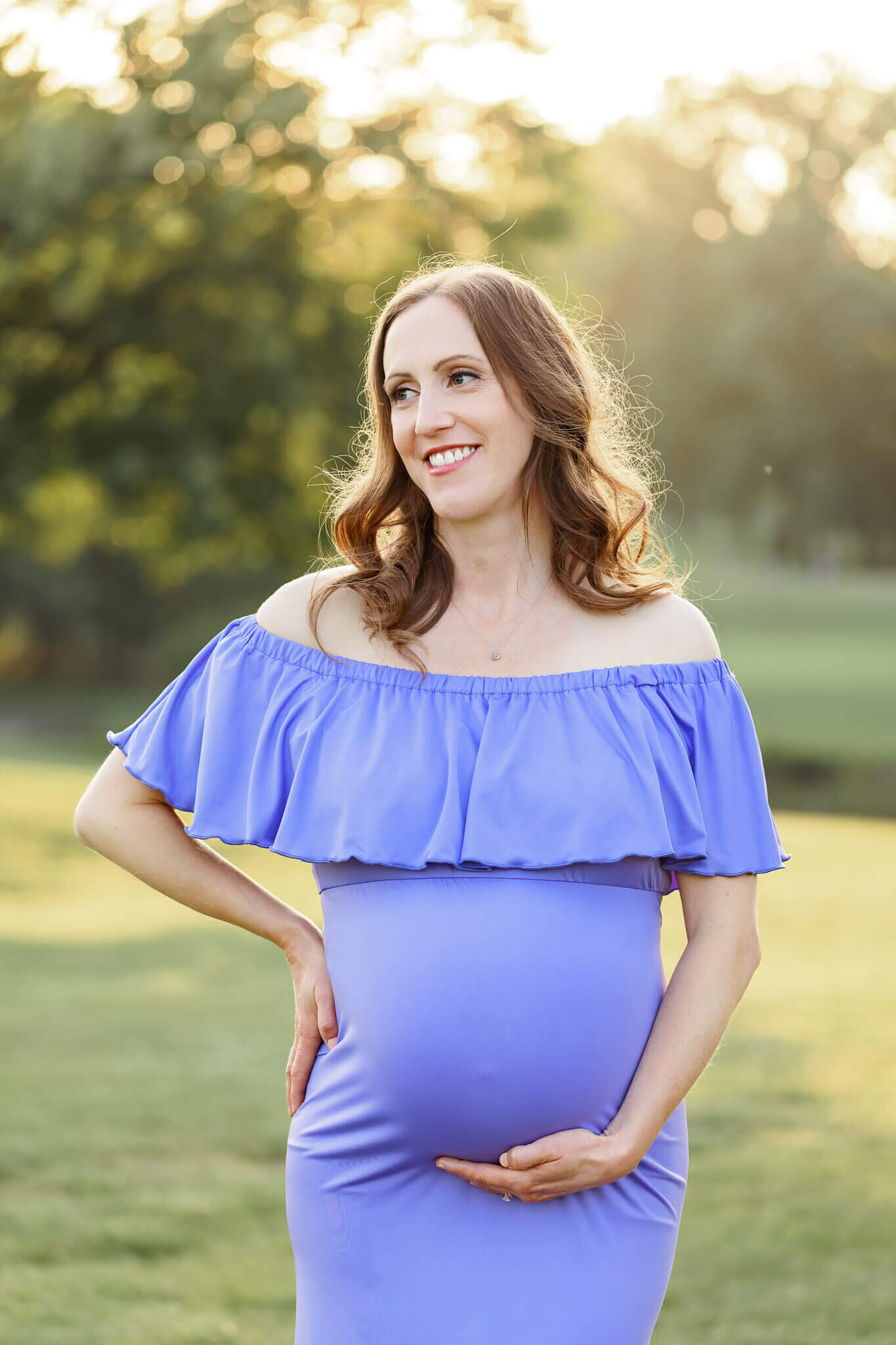 A mom-to-be in a purple dress posing at Burke Lake Park at sunset.