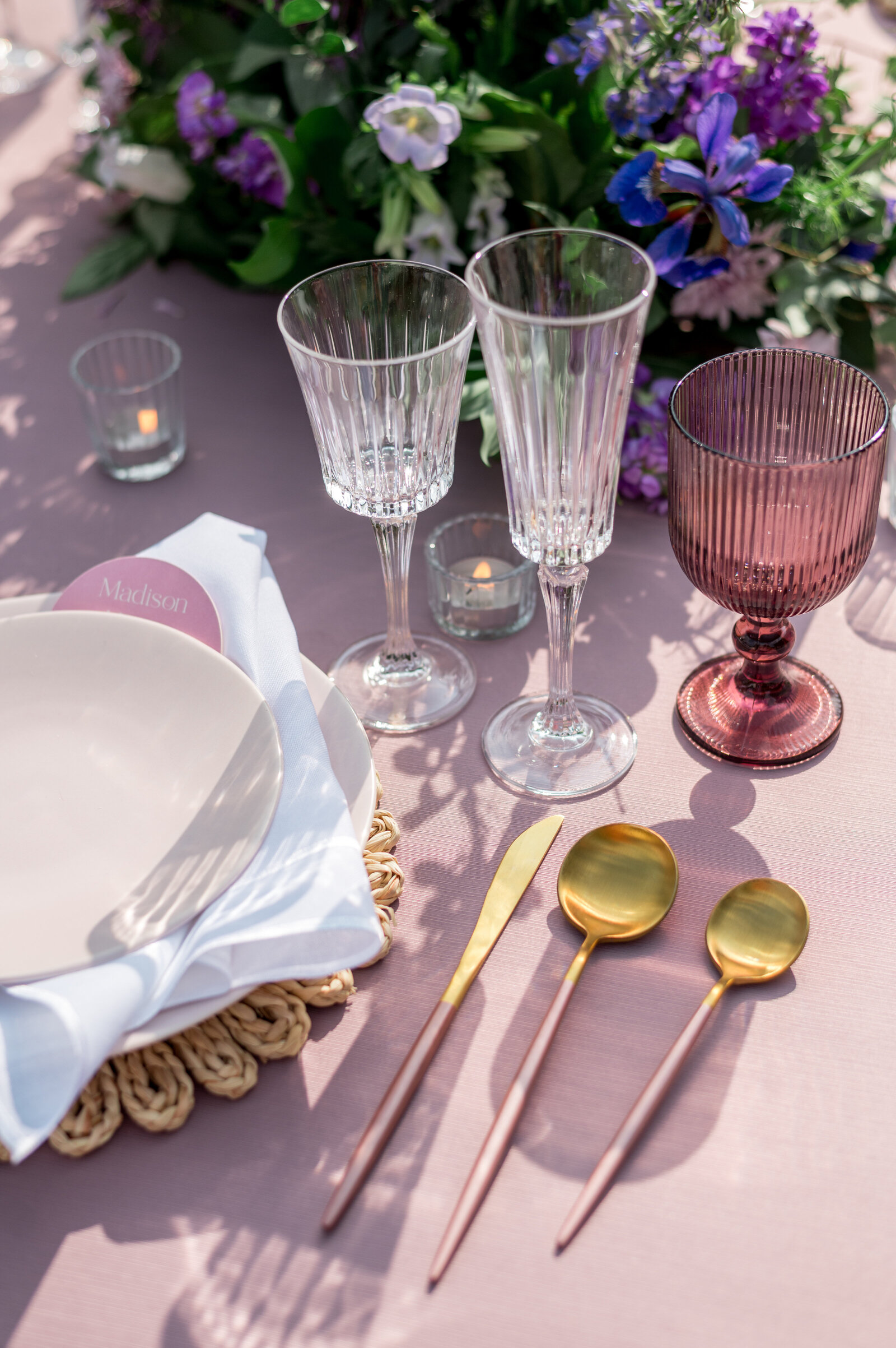 A close-up of a romantic outdoor wedding tablescape featuring blush and gold flatware, layered glassware, soft lavender florals, and natural woven textures — airy, colorful, and effortlessly luxurious at Willowdale Estate. Designed by Events by Elise.