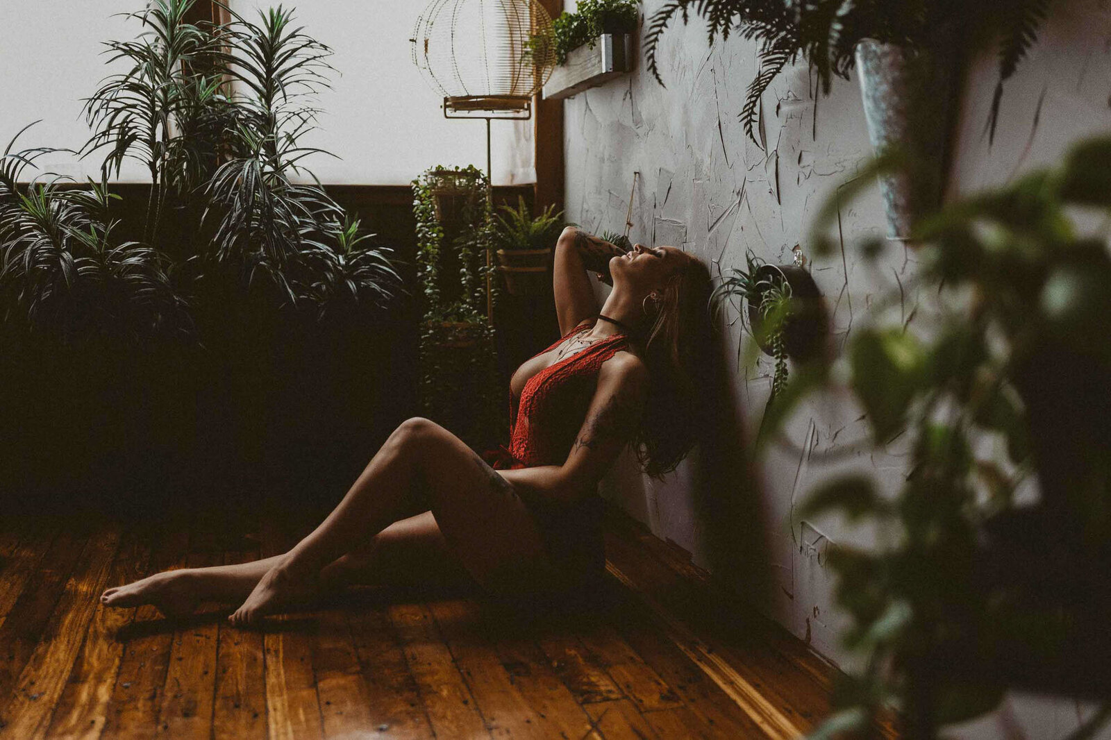 Woman in red lingerie sitting on the floor, surrounded by indoor plants
