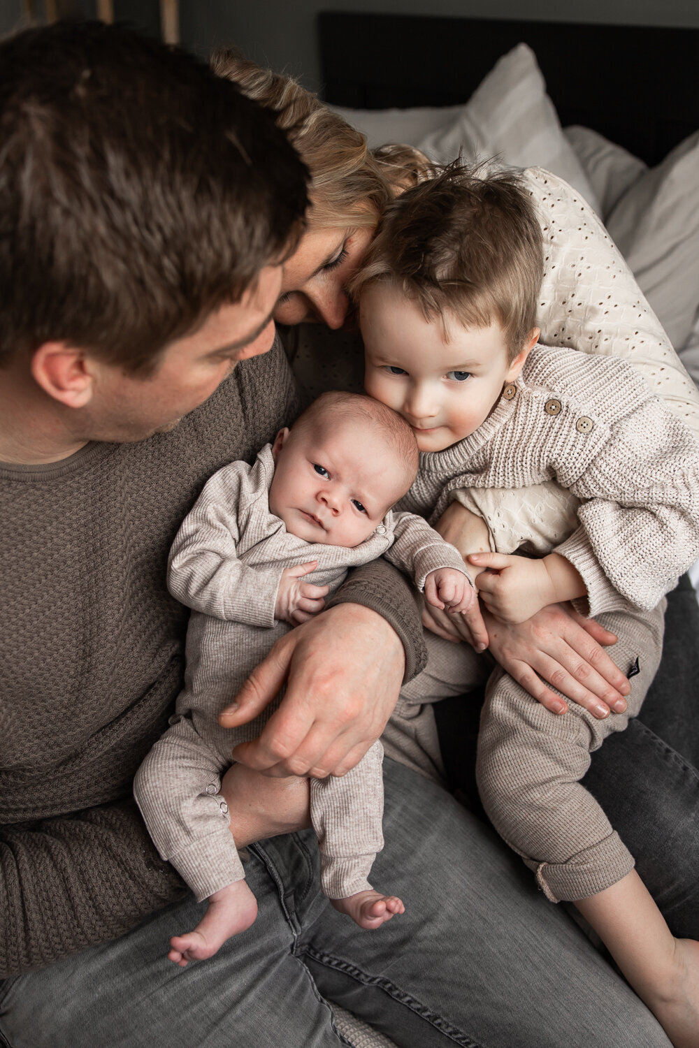 Grote broer knuffelt samen met zijn ouders zijn babybroertje - newbornshoot thuis.
