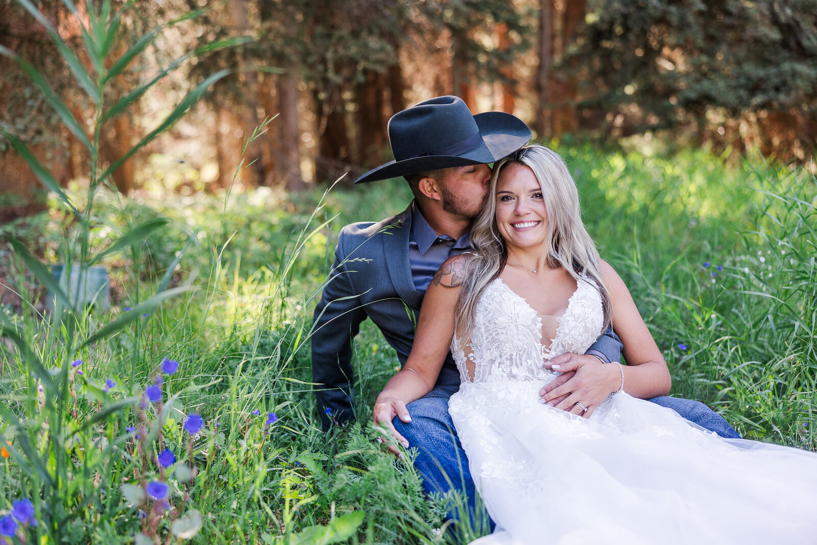 Bride and groom sit in a meadow outside a forest in arrowhead Colorado