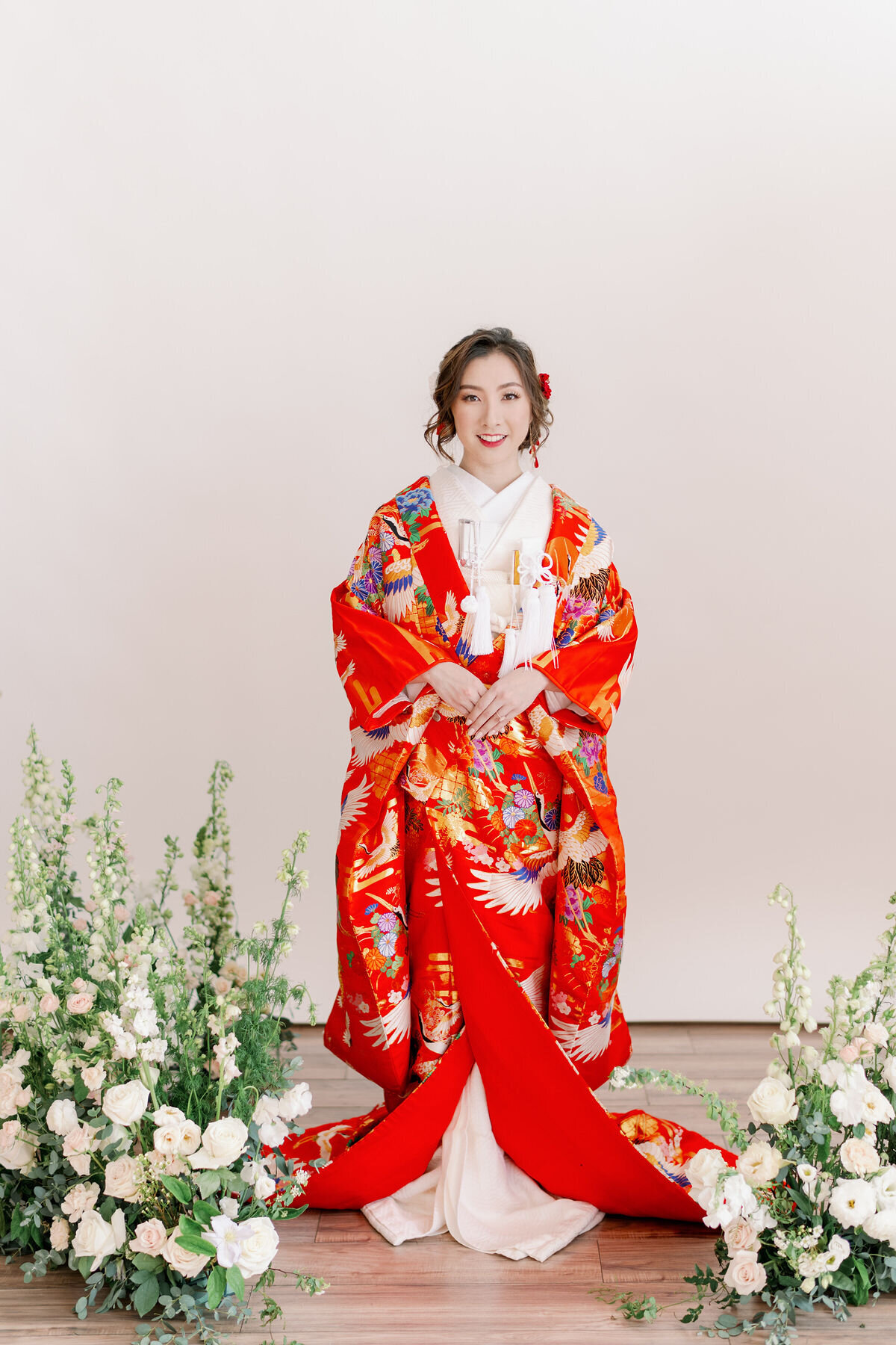 Full-length portrait of bride wearing red iro-uchikake wedding kimono with floral aisle decor in Los Angeles wedding kimono rental studio | 赤い色打掛を着た花嫁の全身ポートレート、フラワー装飾 ロサンゼルス着物レンタルスタジオ撮影 