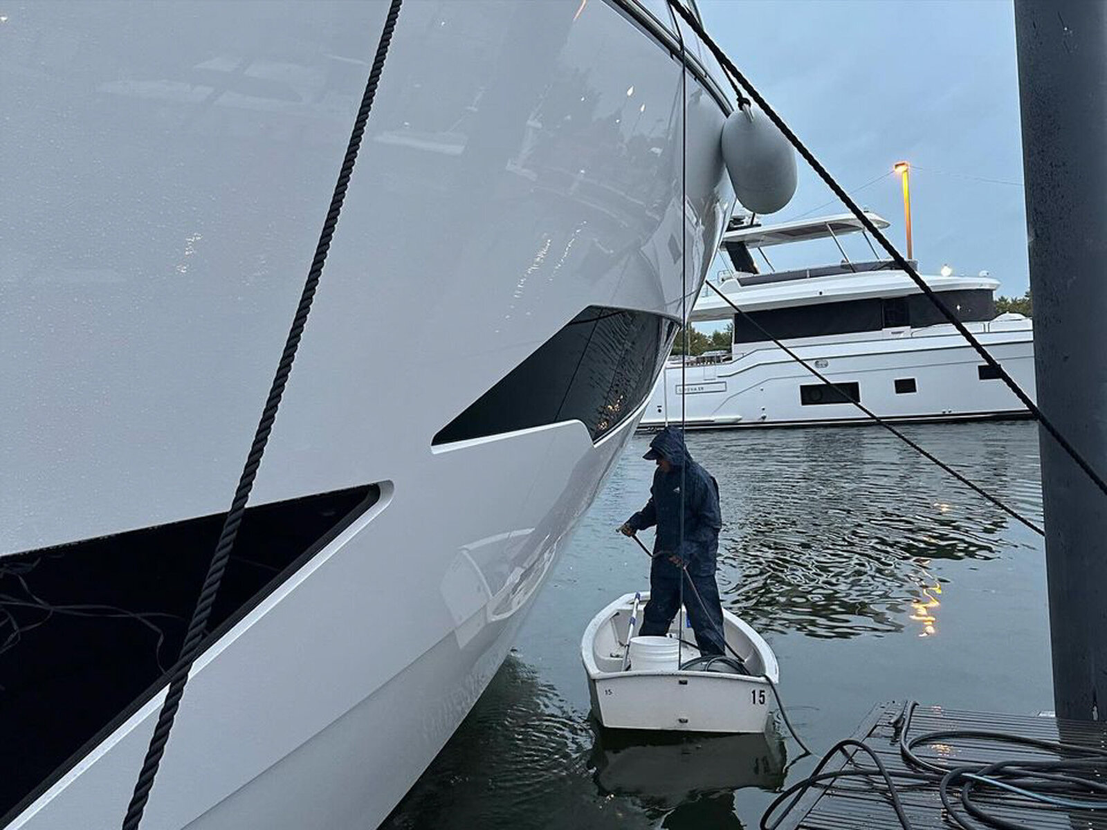 Worker cleaning the side of a yacht from a small boat